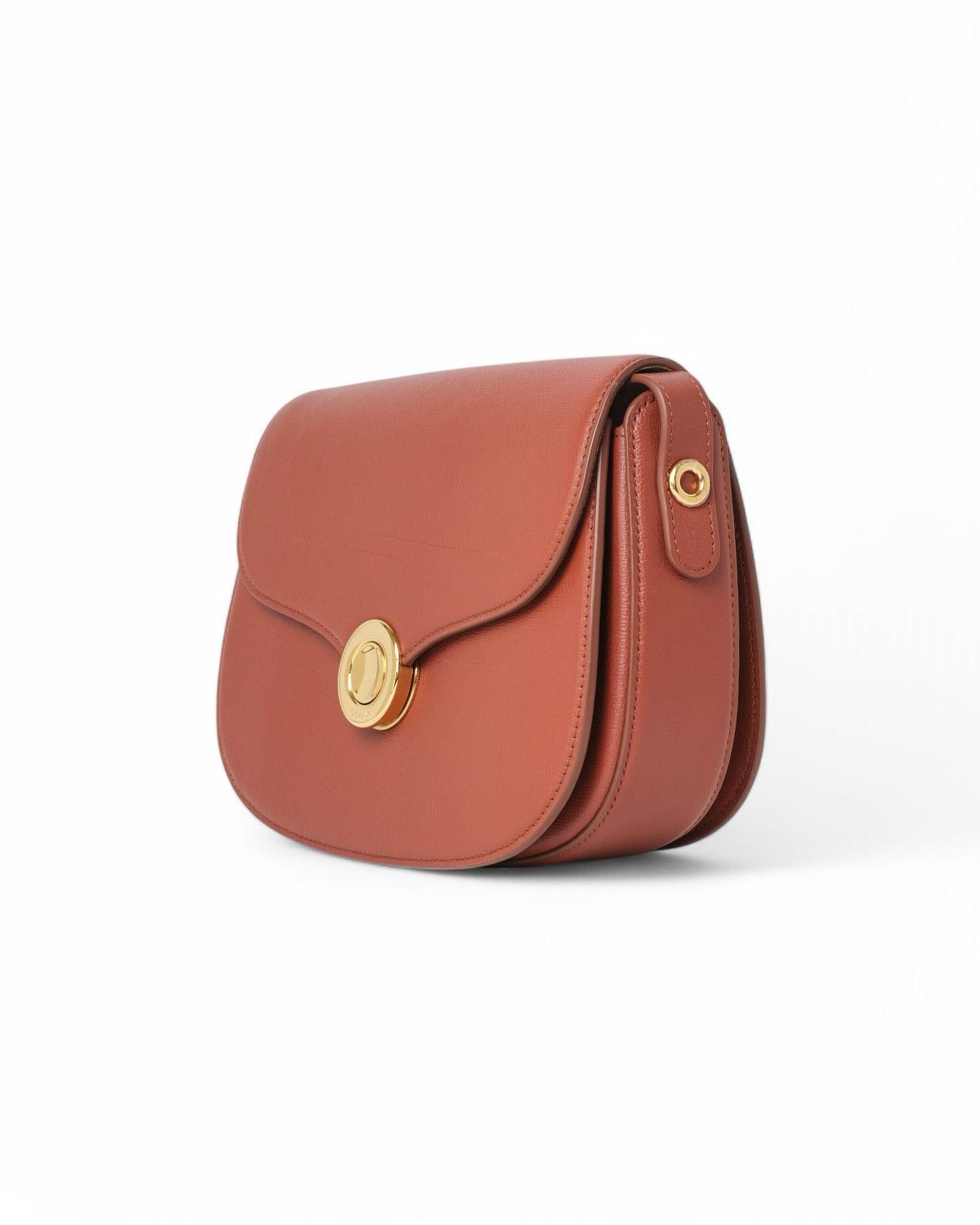 Borsa firmata Loro Piana, modello Ghiera nella misura Small, realizzata in pelle martellata nella colorazione mattone con hardware dorati. Dotata di una patta frontale con chiusura ad incastro, internamente rivestita in tessuto scamosciato beige con