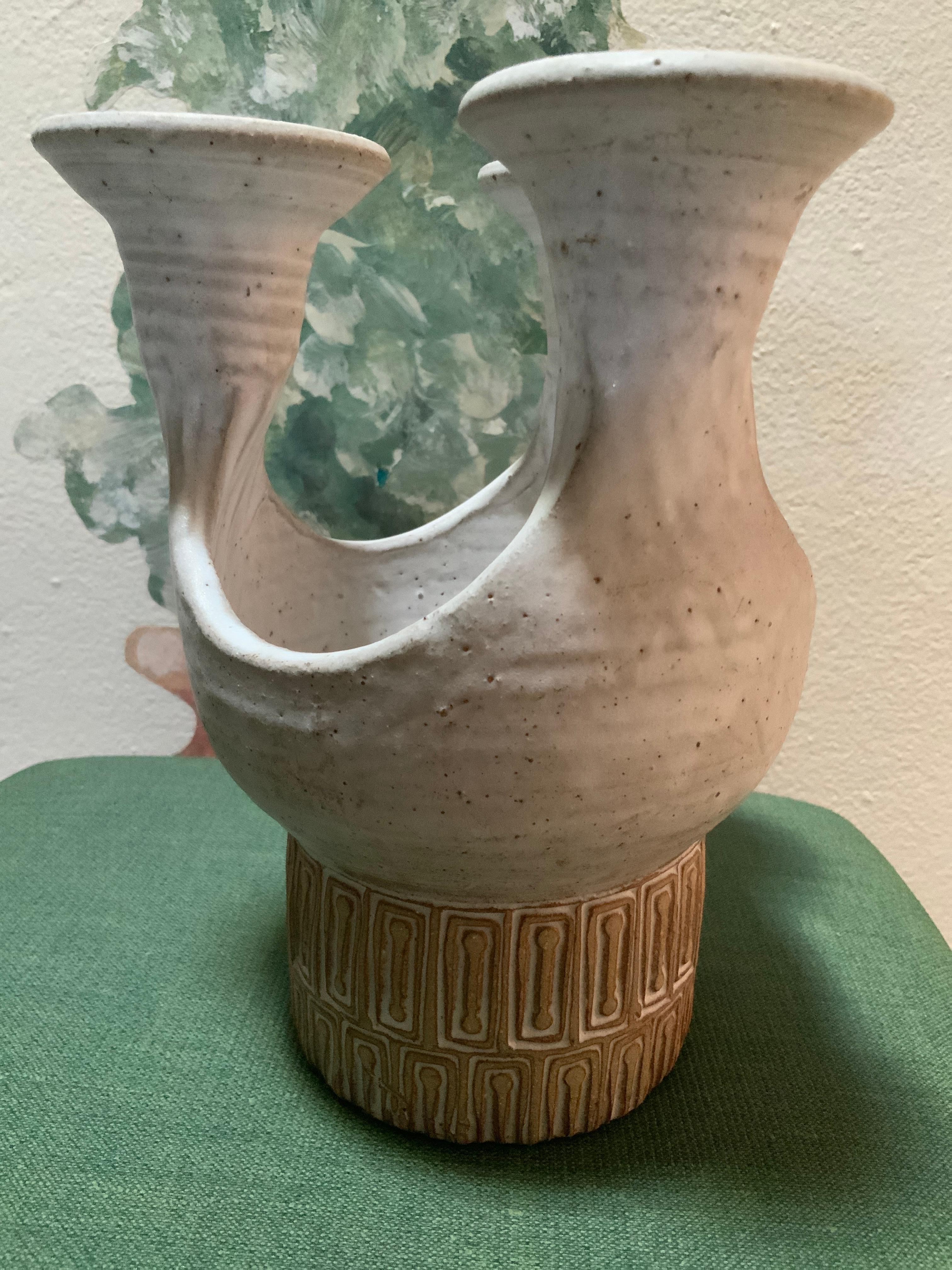 This is a Puerto Rican Los Artesanos Pottery Candleholder Centerpiece. It depicts a white color ceramic trumpet shaped three arms candleholder with a center bowl like base. The base is adorned by a geometric pattern of brick color rectangles. Below