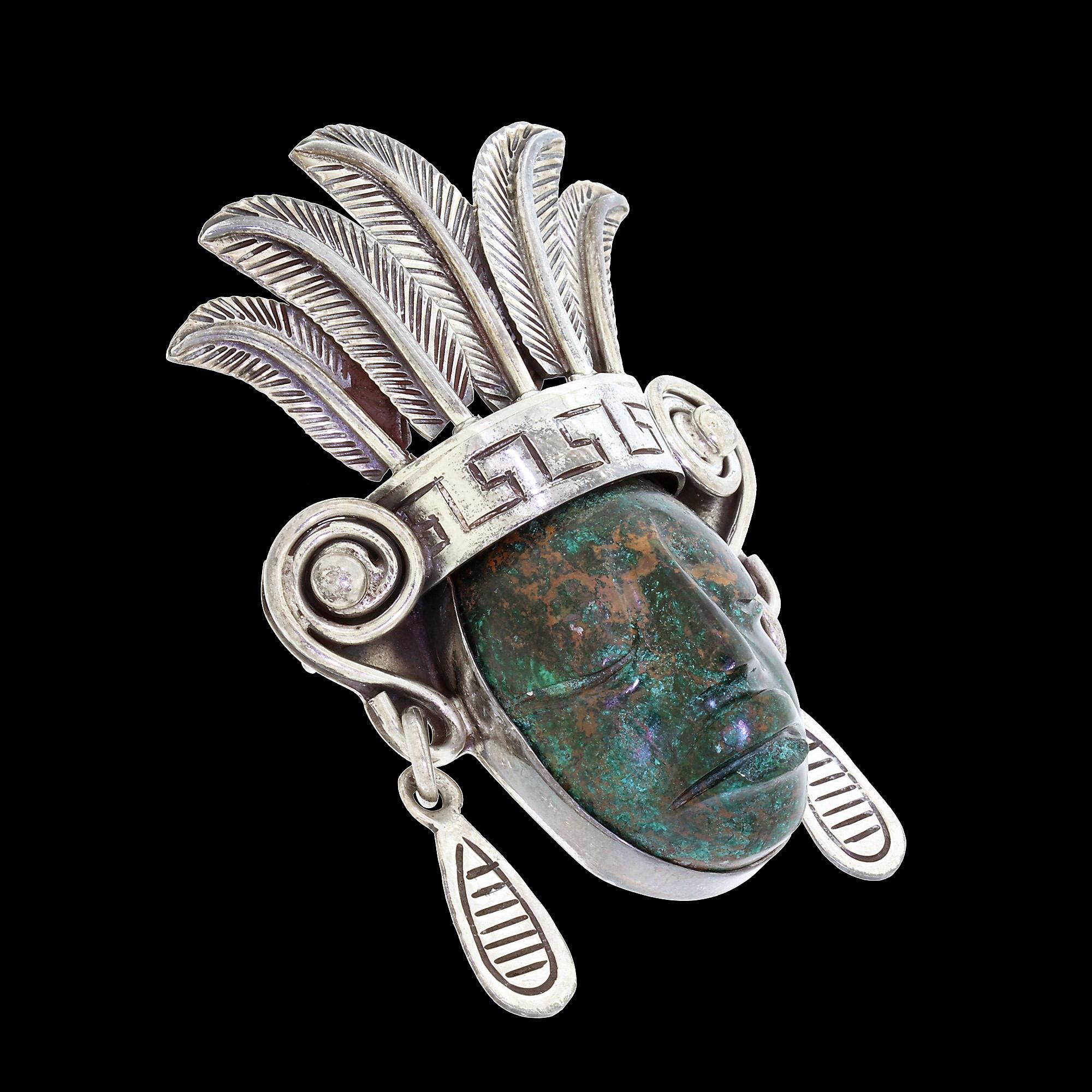 This is an early, rare, and important Los Ballesteros sterling silver and carved turquoise brooch of exceptional quality. 

The pin features an intricately designed motif of a Mayan face wearing a ceremonial feather headdress. The plumed headdress