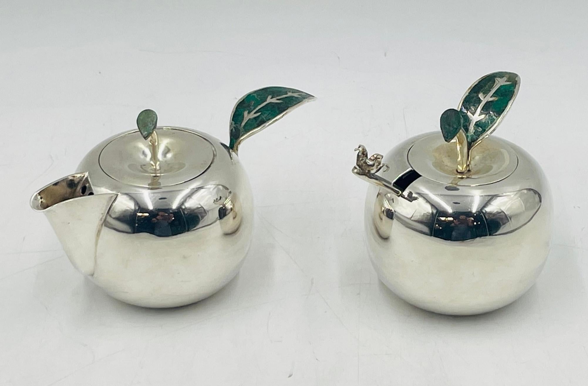 A playful yet refined silver plated apple-form service set by Emilia Castillo for Los Castillo, crafted in Taxco, Mexico in the late 20th century. This collectible set includes a creamer pitcher, lidded sugar pot, and matching ladle, each