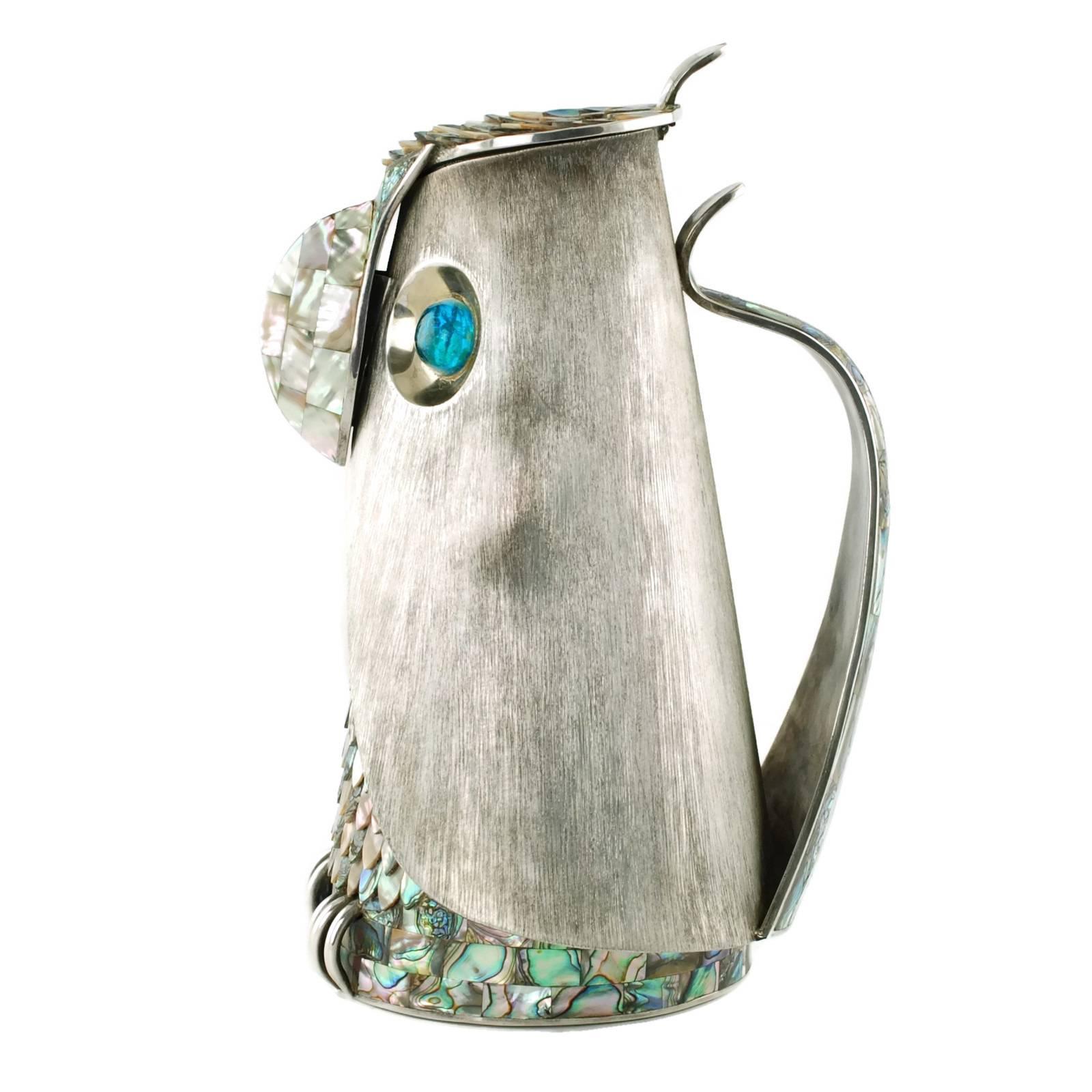 This MCM lidded pitcher was made by highly regarded taller Los Castillo of Mexico. The piece has been made in the form of a stylized owl and features a brushed silver plate exterior along with abalone accents in the form of overlapping feather