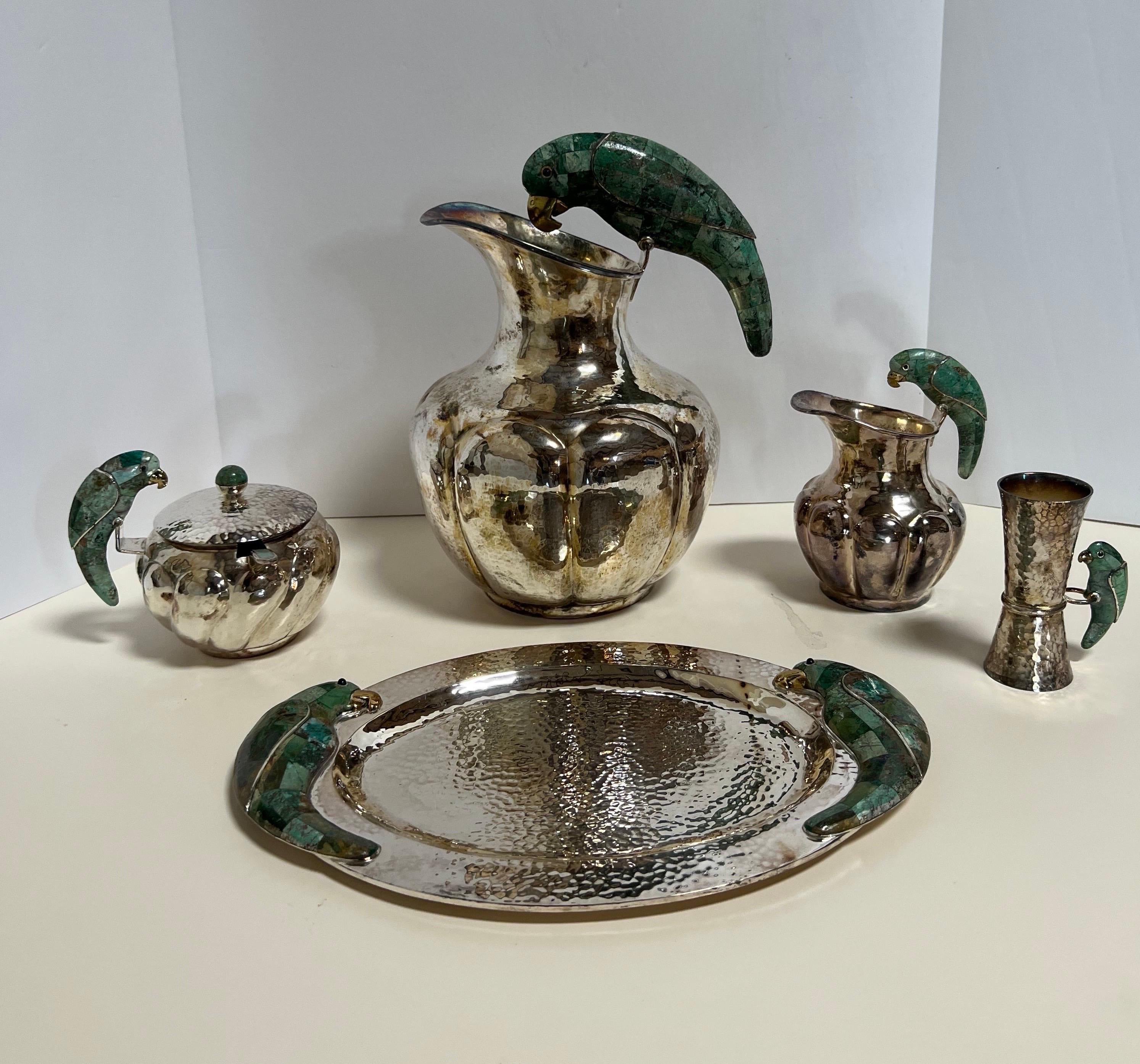 A very fine five-piece hammered silver plate serving set by Los Castillo featuring a malachite parrot motif.

Taxco, Mexico, circa 1950.

All pieces are signed/stamped.

Includes the following 5 pieces:

1. Pitcher

2. Tray

3. Creamer

4. Sugar