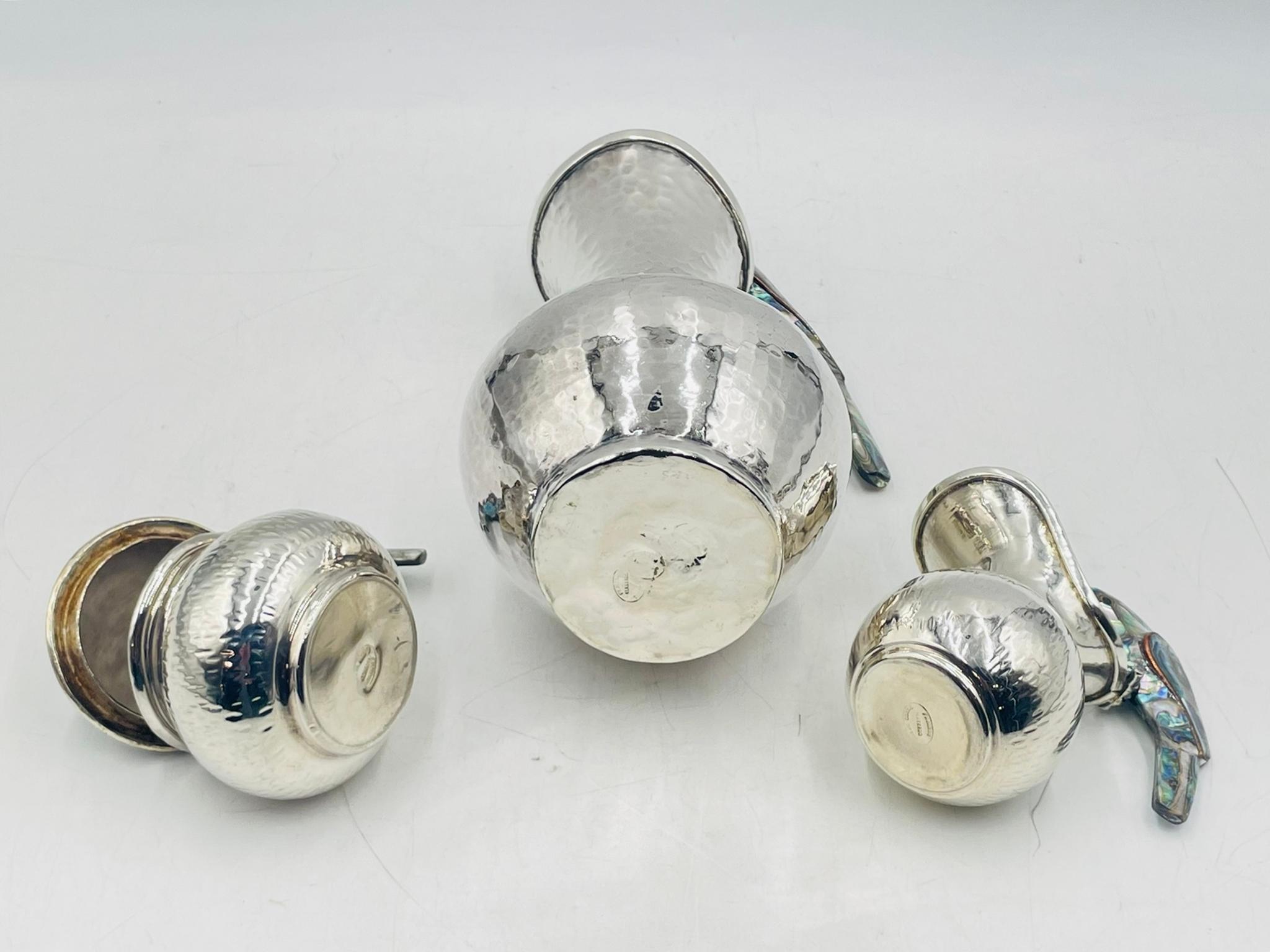 A rare and striking three-piece silver plated service set by Los Fajardo, crafted in Taxco, Mexico, during the 1960s. This sculptural ensemble includes a water pitcher, creamer, and lidded sugar pot, each masterfully hand-hammered in silver plate