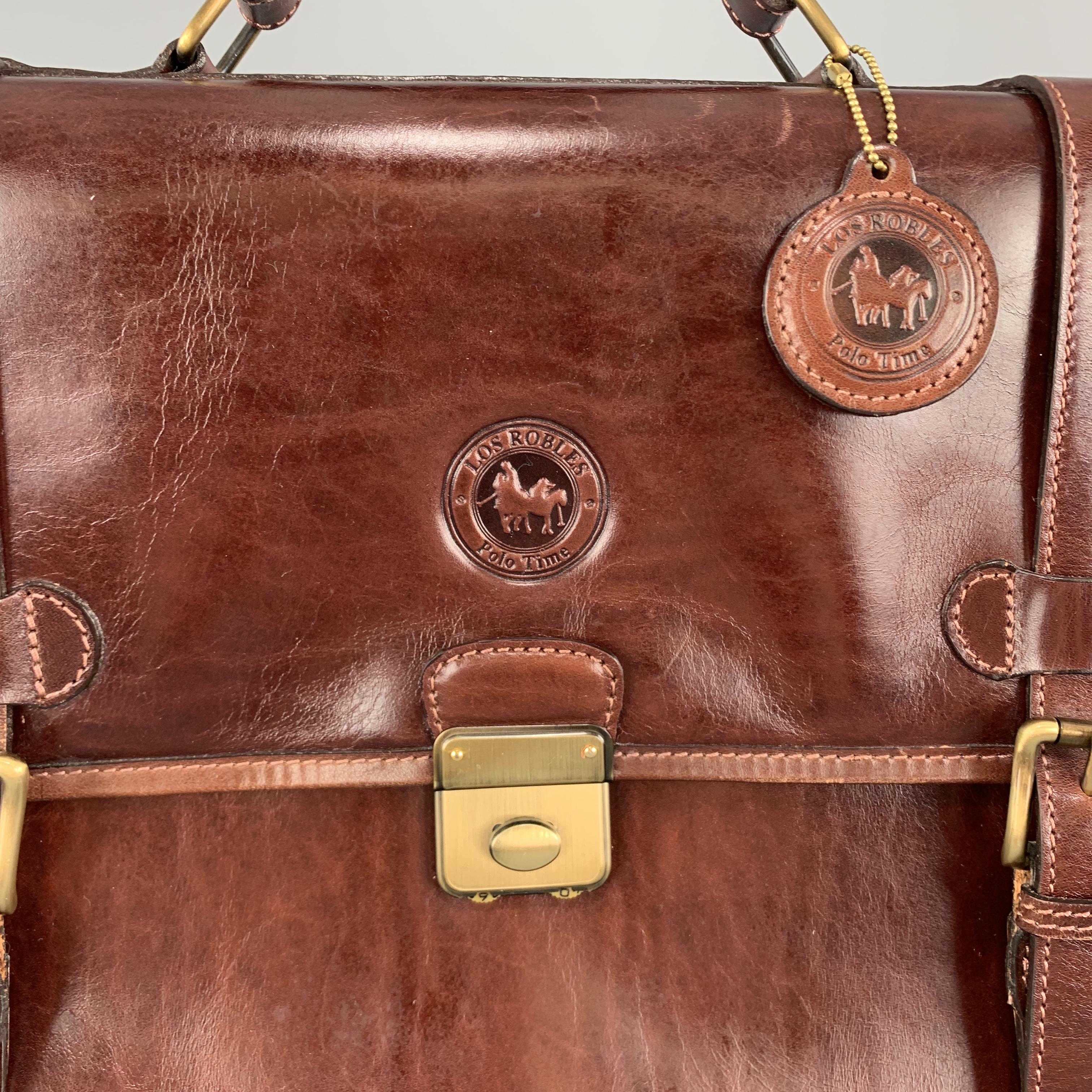 LOS ROBLES POLO TIME briefcase satchel comes in cognac leather with a rolled top handle, flap, double buckle and lock closure, detachable strap, and double compartment interior with storage pockets. Wear throughout. 

Good Pre-Owned