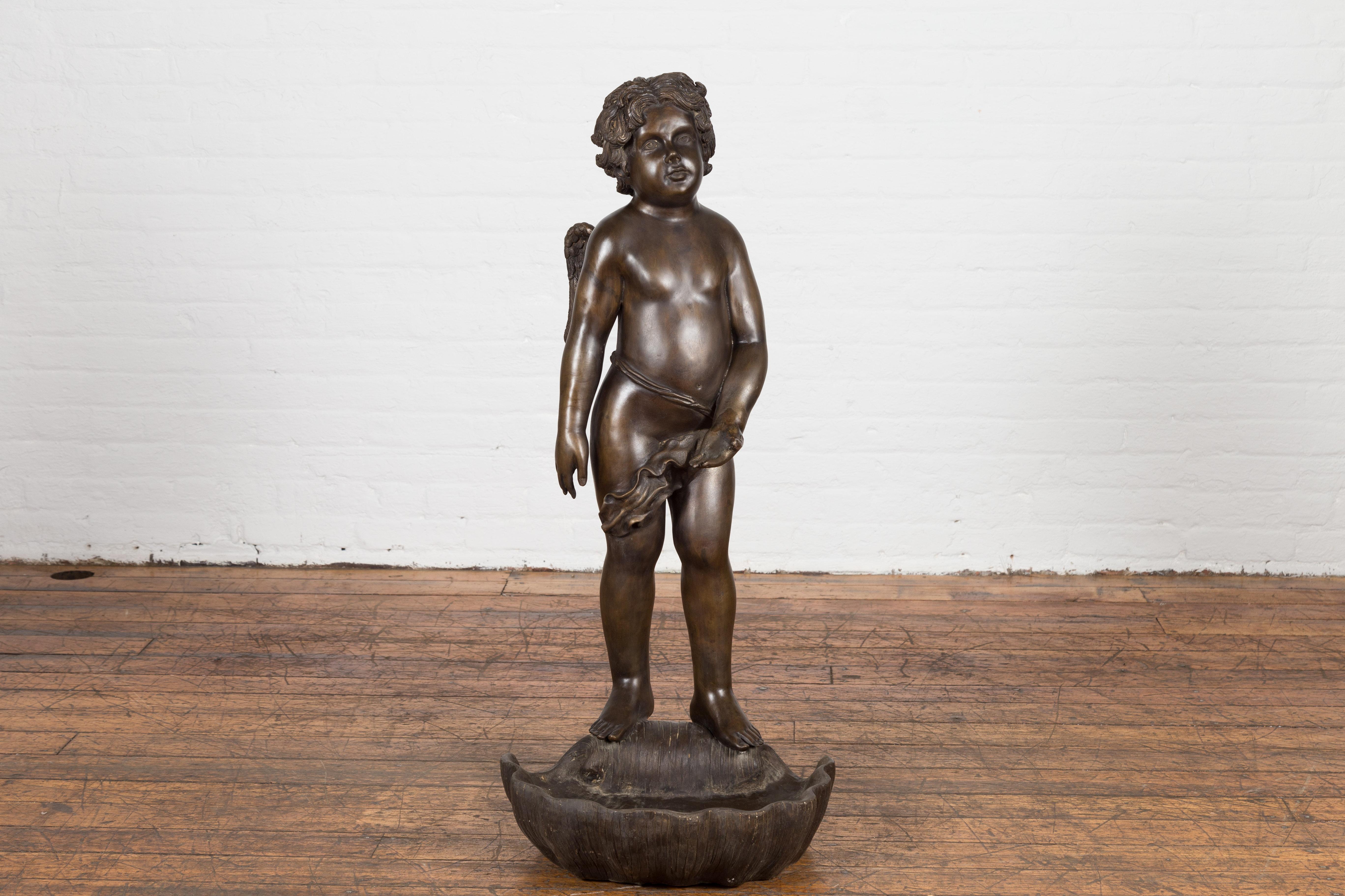 A vintage Greco-Roman style lost wax cast bronze statue of a cherub standing on a shell from the 20th century, with great details in the curly hair, chubby face and wings, in dark patina. This vintage Greco-Roman style statue beautifully captures