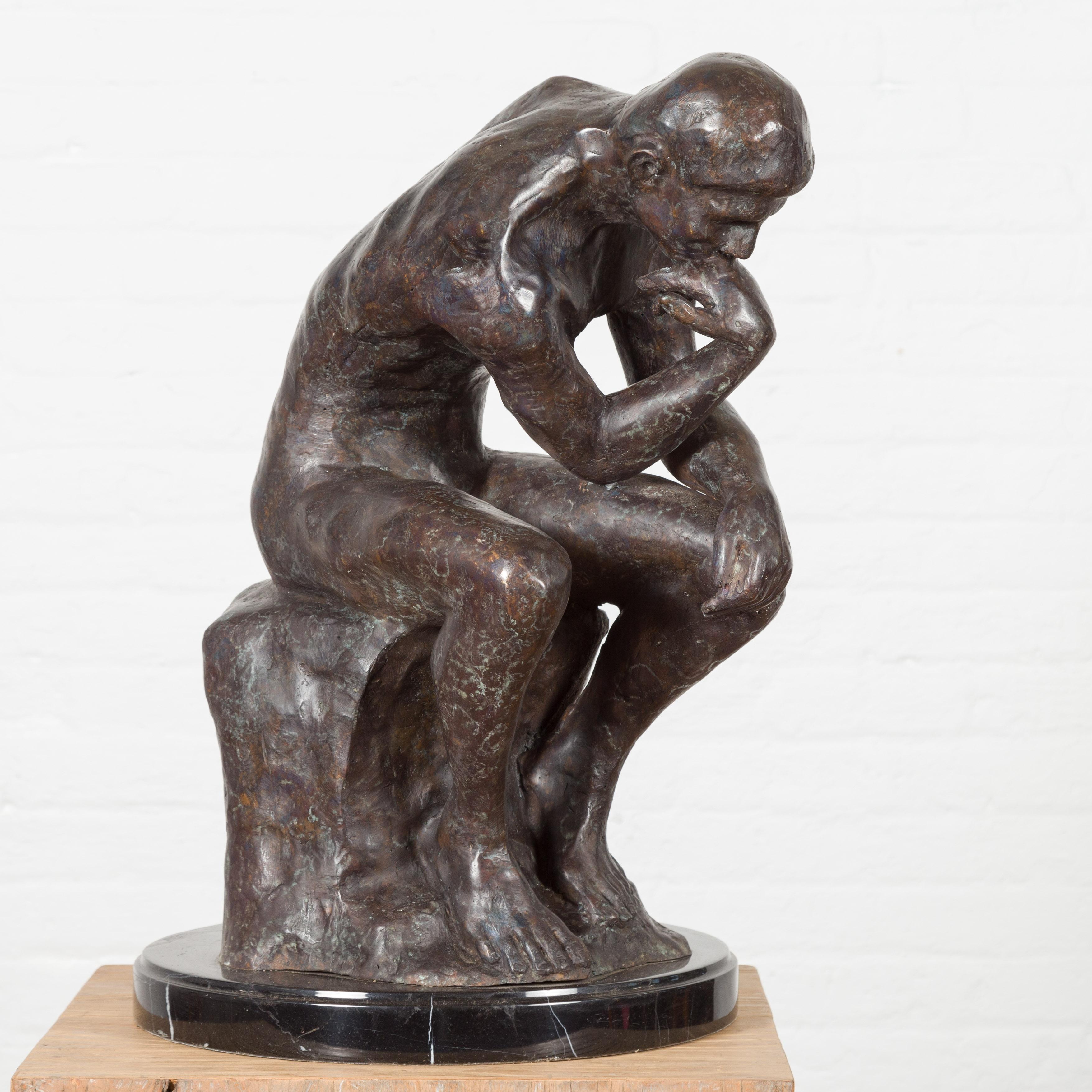 A lost wax cast bronze sculpture, inspired by Auguste Rodin's The Thinker, in dark patina on black marble base. This item is available now and this is also a current production. Created with the traditional technique of the lost-wax (à la cire