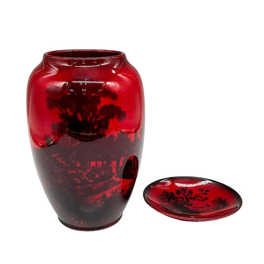 Deep red glazed vase with a scene of a house next to trees, shrubbery, and an open glade, 6.75