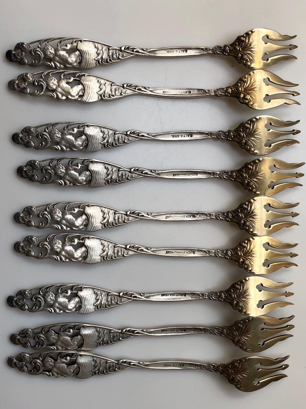 Lot of 9 sterling silver forks with gold washed tines and openwork figural handles depicting a puti figure in a boat and a fish below. Each measures 5.5