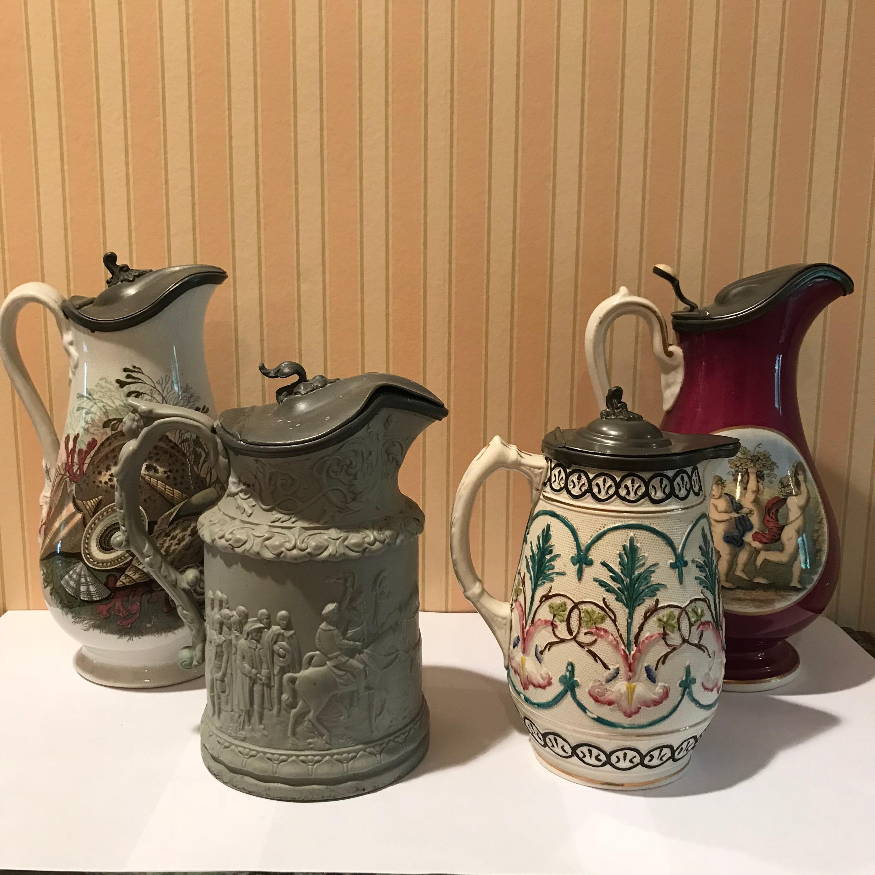 Lot of four (4) Pewter top porcelain pitchers and tankards. Each decorated with floral patterns and figurative scenes. All in excellent condition.
1: M.W.&Co 1860s, H 9.75