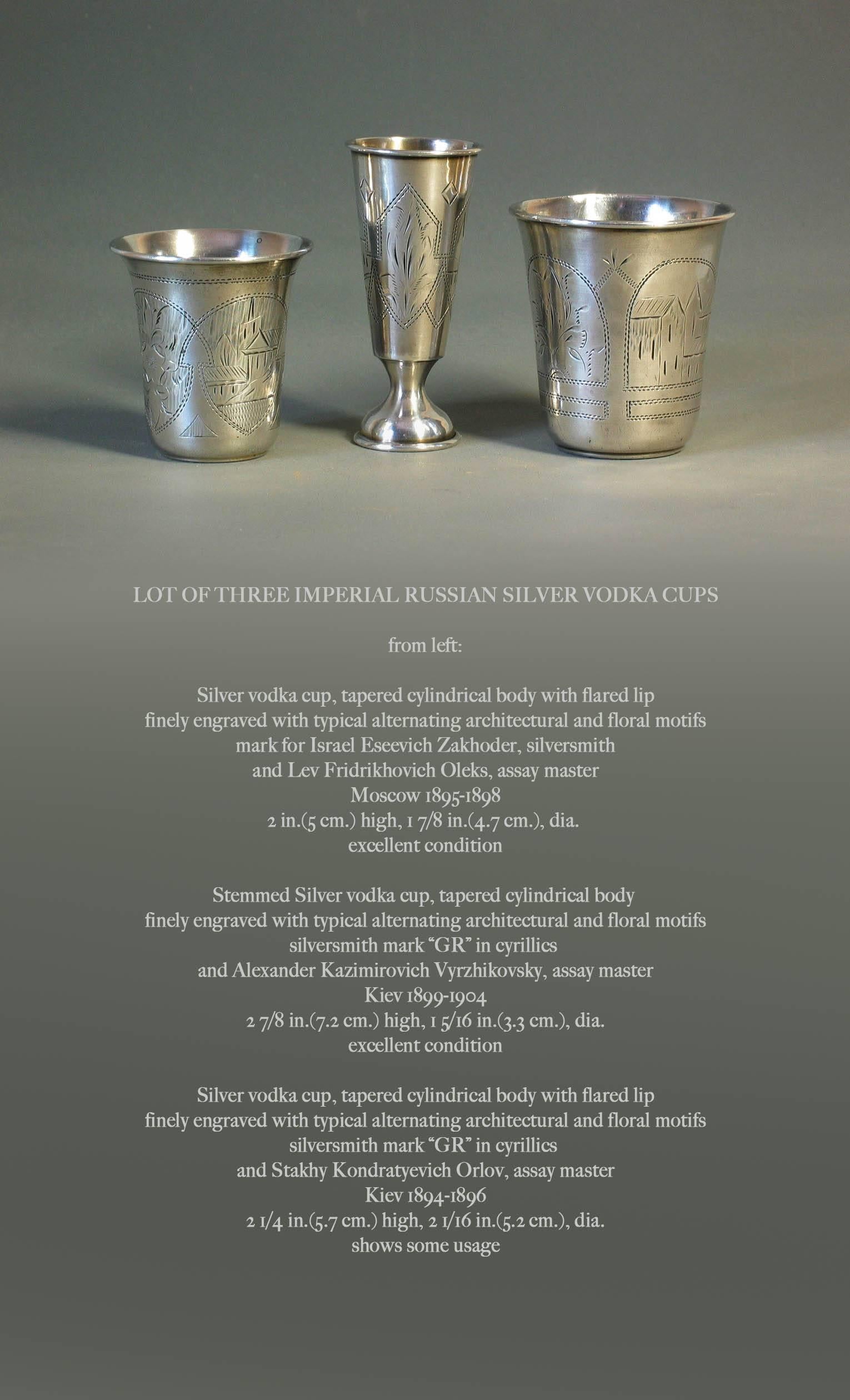 Lot of three Imperial Russian silver vodka cups, 
From the left:
Silver vodka cup, tapered cylindrical body with flared lip, finely engraved with typical alternating architectural and floral motifs. Mark for Israel Eseevich Zakhoder, Silversmith