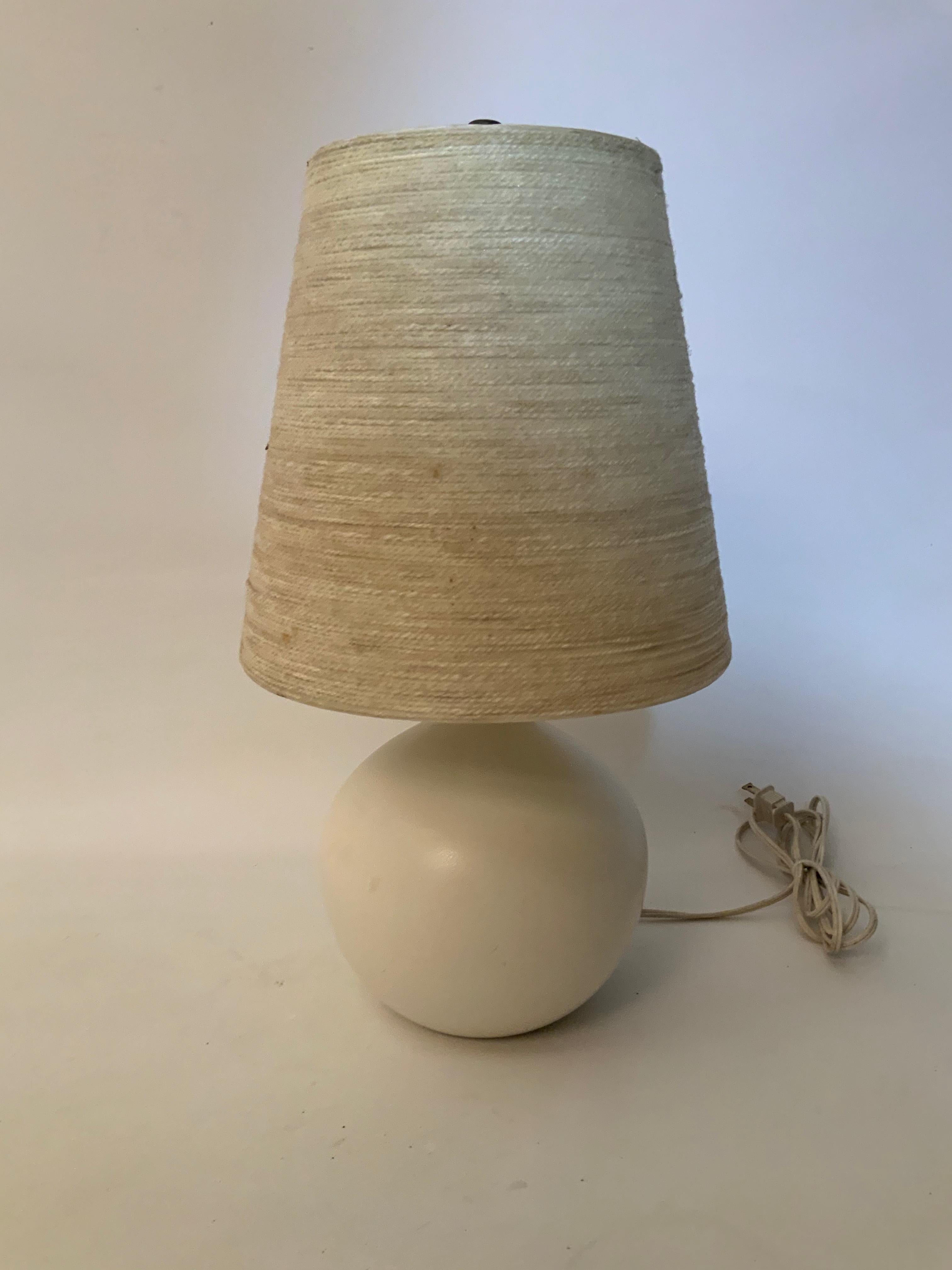 White eggshell finish ceramic table lamp with the original fiberglass shade. Signed with paper label, Bostlund Industries, circa 1960. Very good condition. Felted bottom. Original wiring in good working condition. 

Approximate overall height from