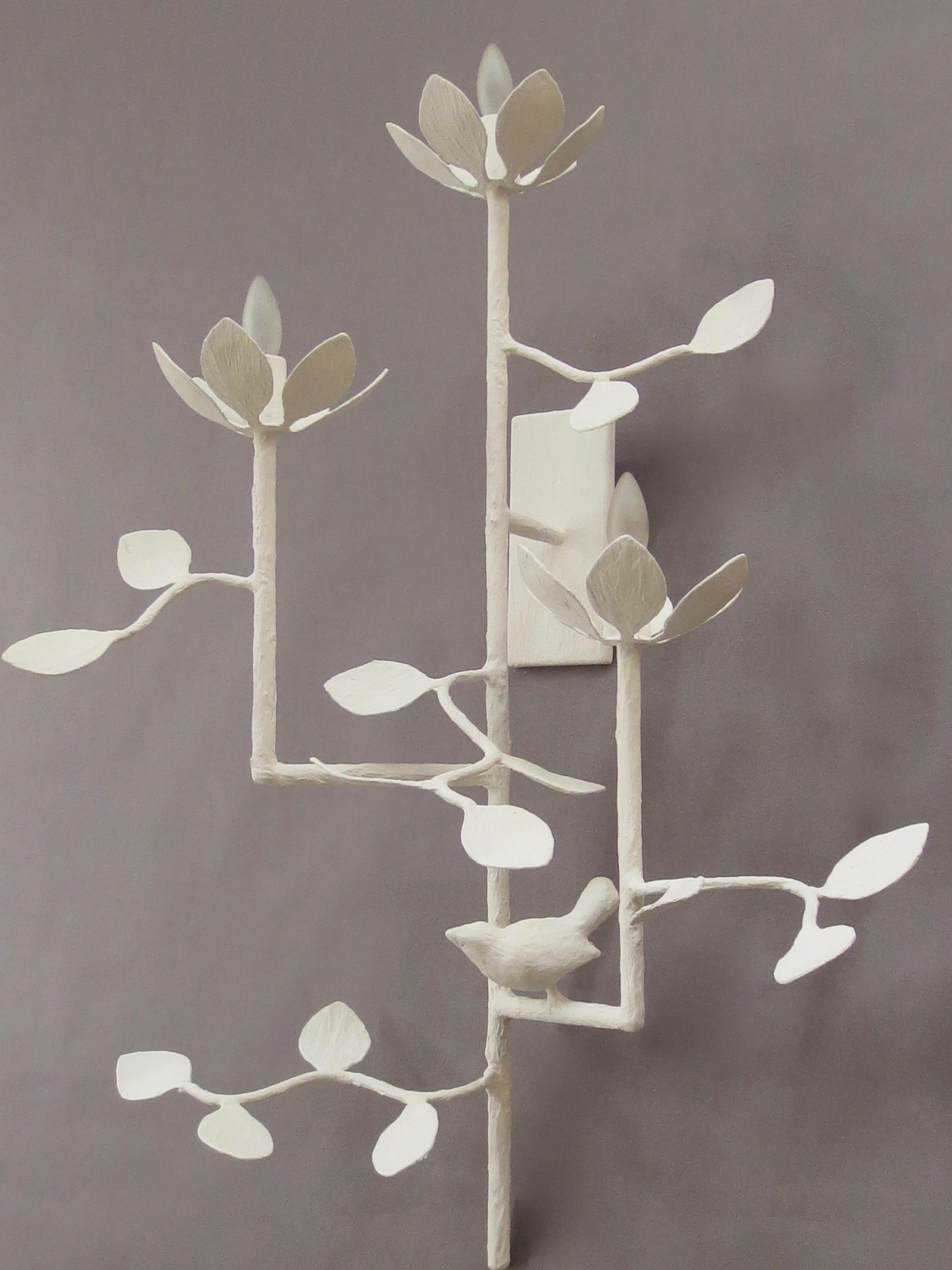 Lotus 3 arm plaster wall sconce by Tracey Garet of Apsara Interior Design includes 3 lights on various levels. A single bird adorns one of the arms and leaves are detailed throughout. The 3 lotus flowers each contain a candelabra light. The