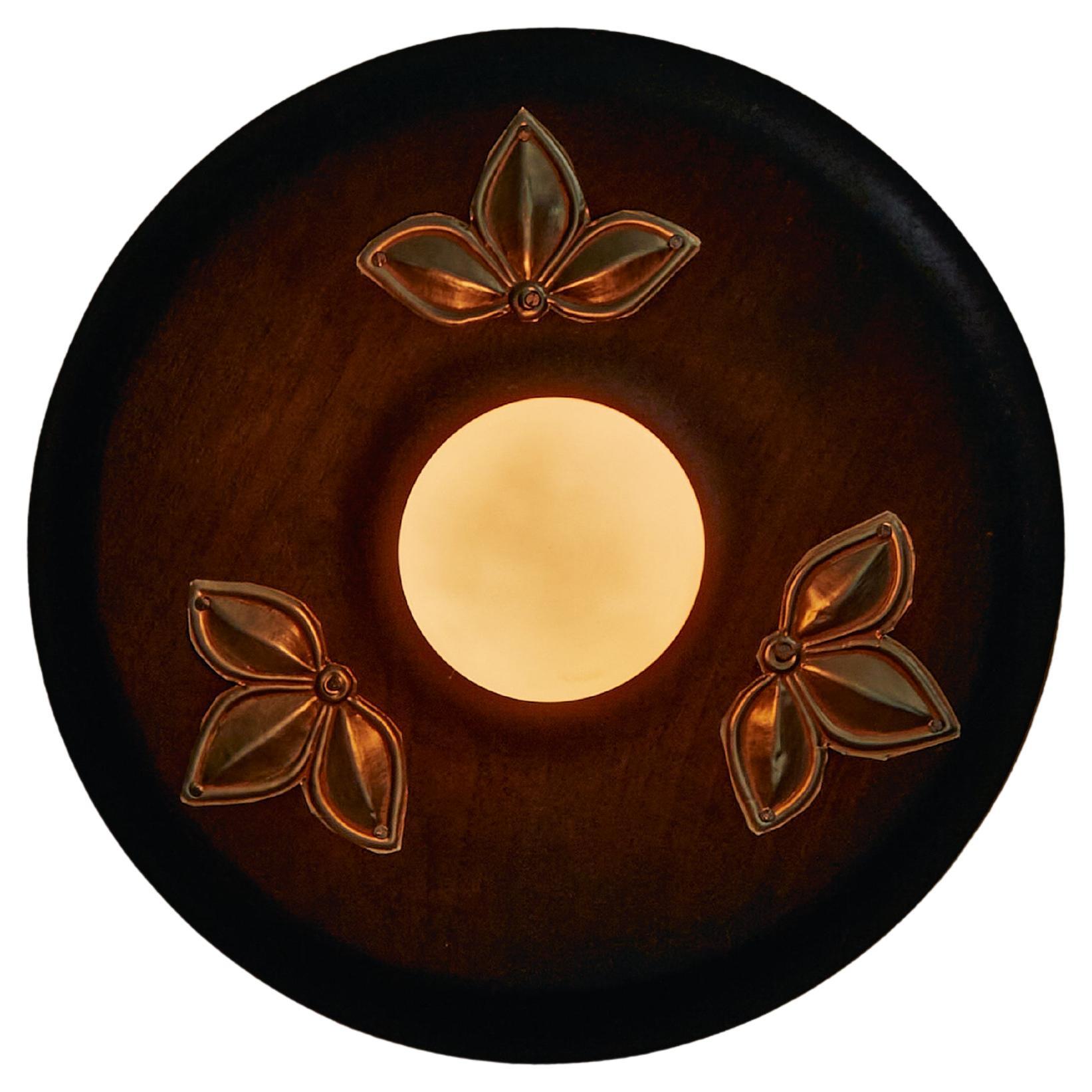 L'applique Mother est une ode à la lumière et à l'éducation. Fabriqué à partir de teck récupéré et incrusté de nacre, il équilibre la chaleur de la terre avec l'éclat céleste. La forme ronde, incrustée de délicats motifs floraux étoilés, rappelle