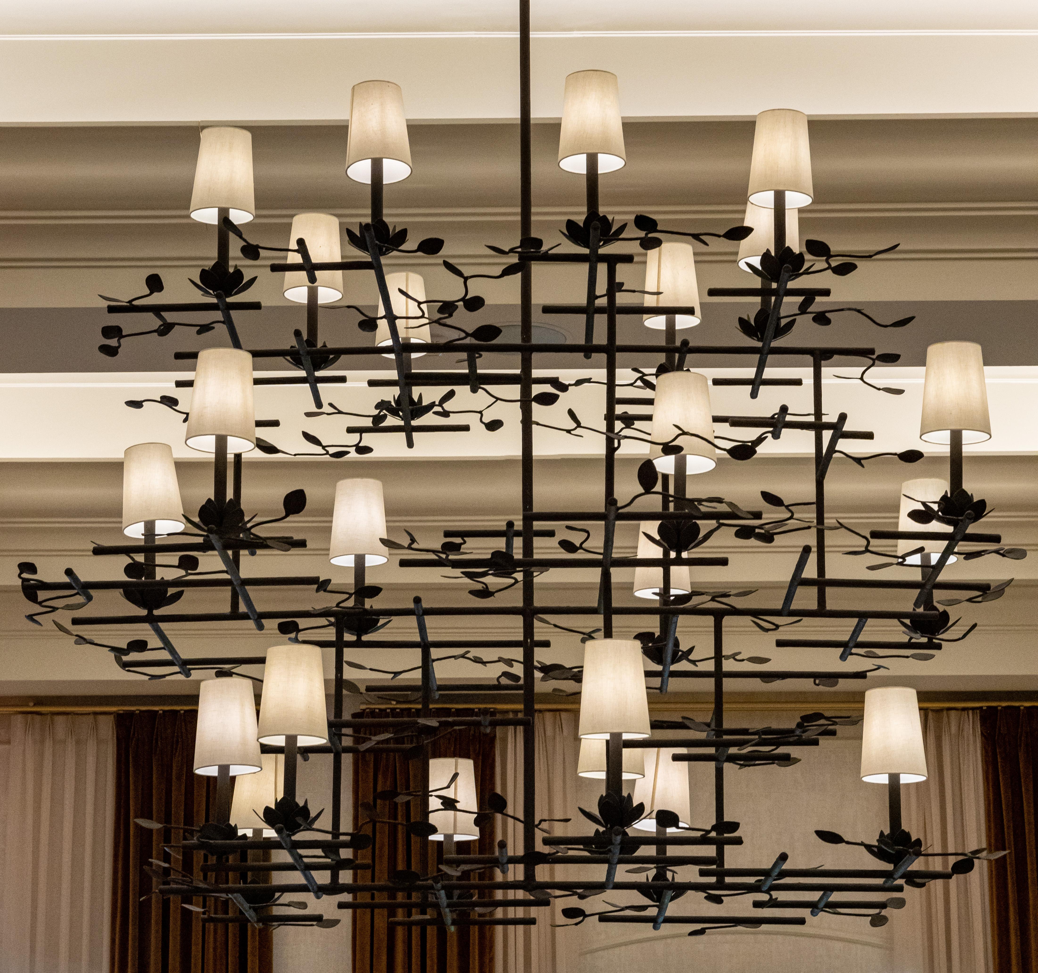 Stunning bronzed finished lotus chandelier with light shades by Tracey Garet of Apsara Interior Design. The chandelier has multiple tiers and 24 lights. Each light rises out of a lotus flower and is surrounded by leaves and branches.  The