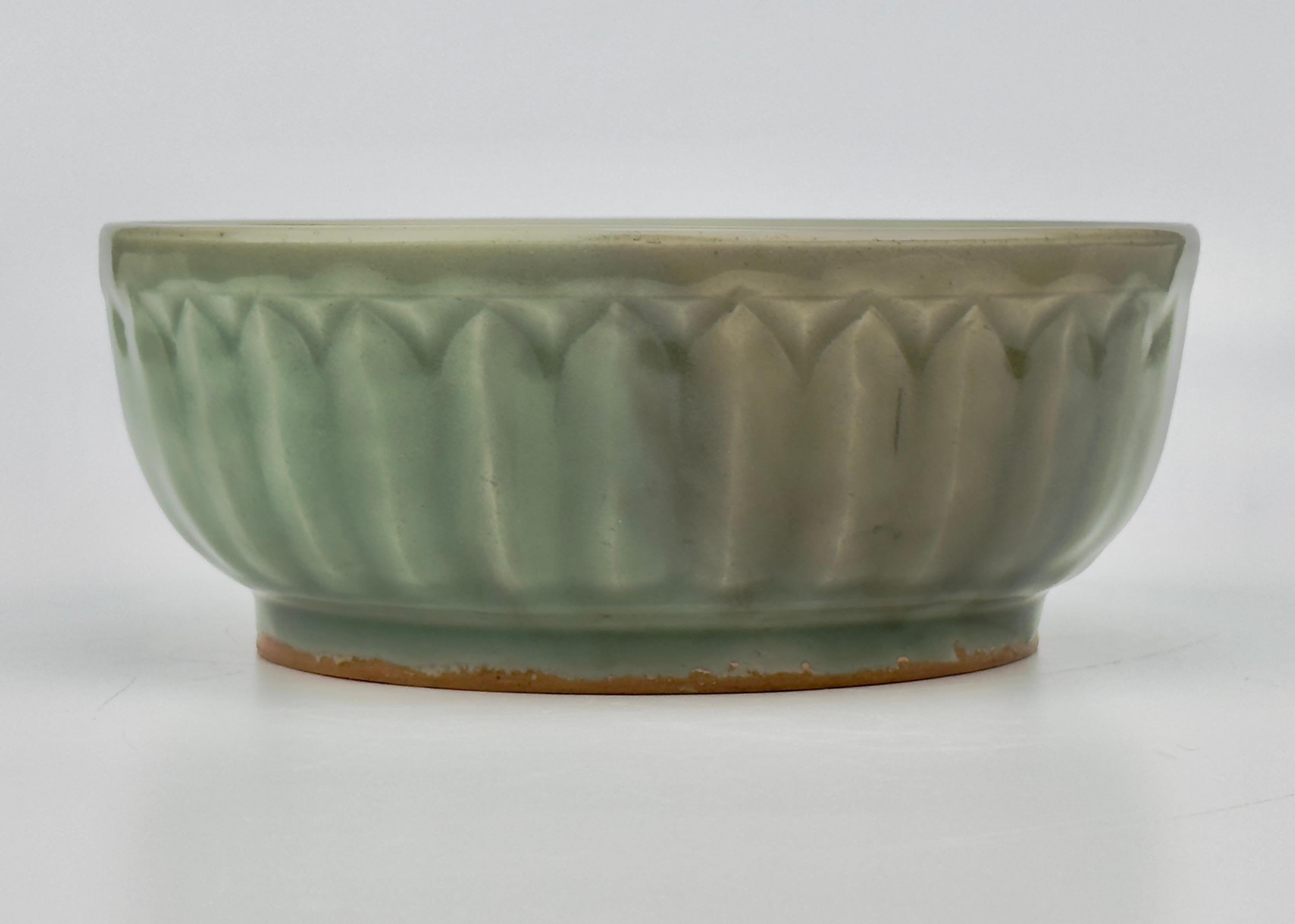 The bowl features a relatively deep green glaze and a smooth and lustrous finish. The exterior is intricately incised with a lotus petal design, symbolizing purity and spiritual enlightenment, while the interior remains plain to emphasize the