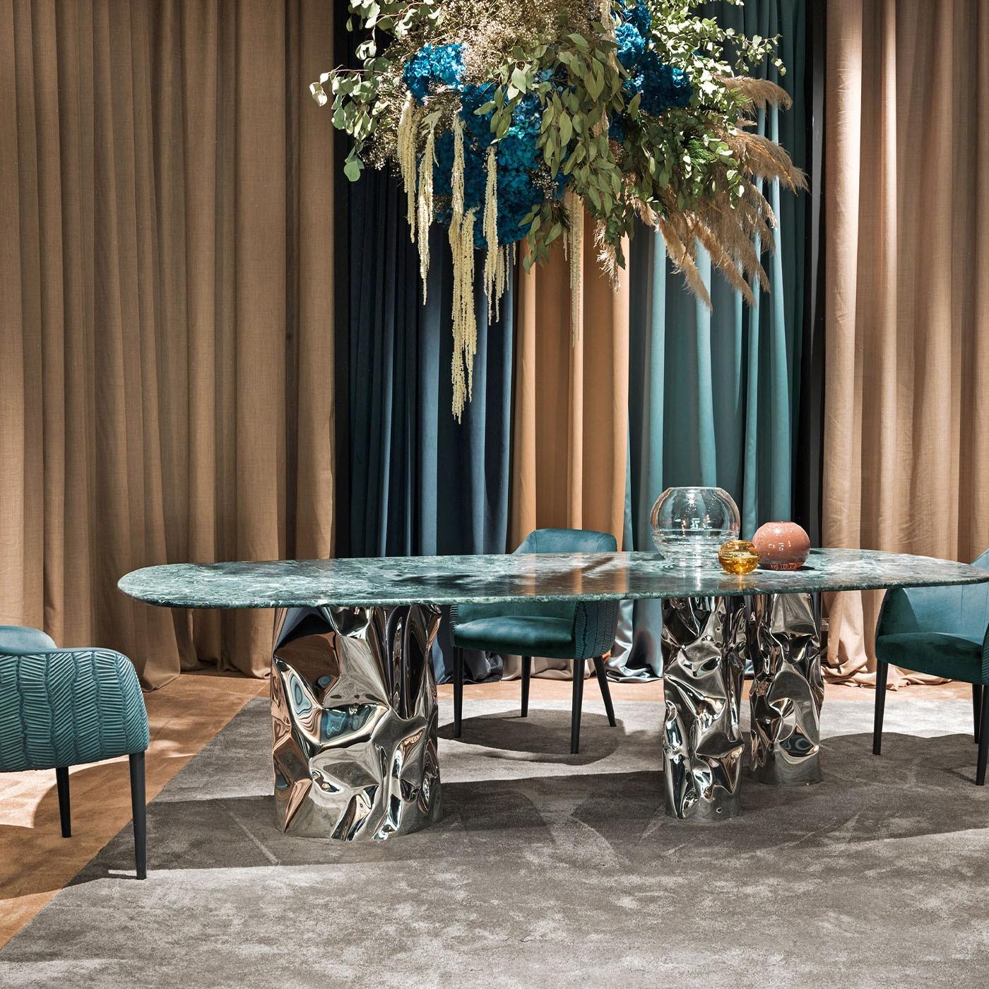 Cette table de salle à manger, qui ne manquera pas d'occuper le devant de la scène dans les intérieurs contemporains, combine audacieusement des textures et des inspirations contrastées. Le majestueux plateau incurvé en marbre Verde Alpi est soutenu