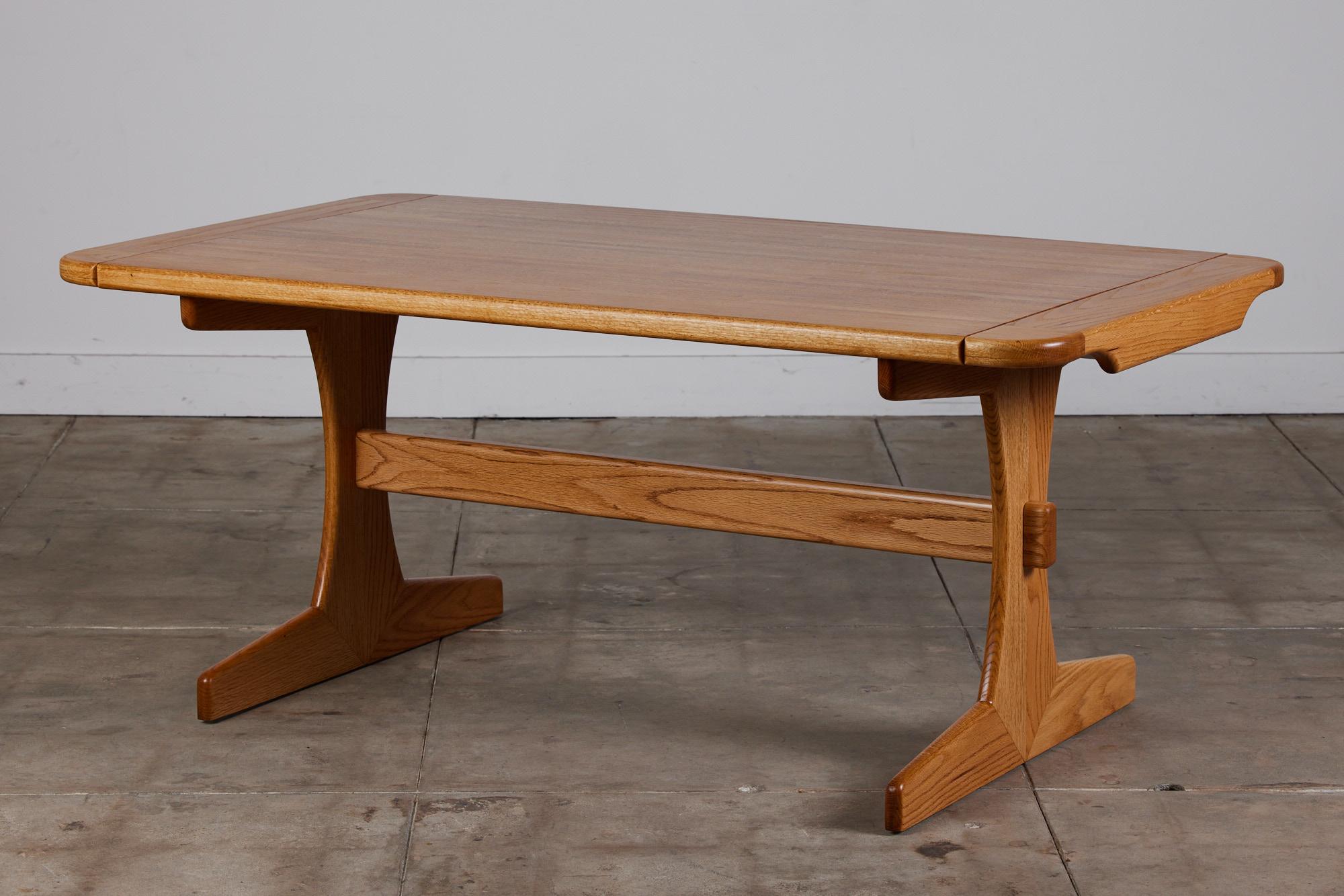 Lou Hodges oak dining table for California Design Group, circa 1970s, USA. This table features a solid oak table top and trestle base. The table comes with two 13