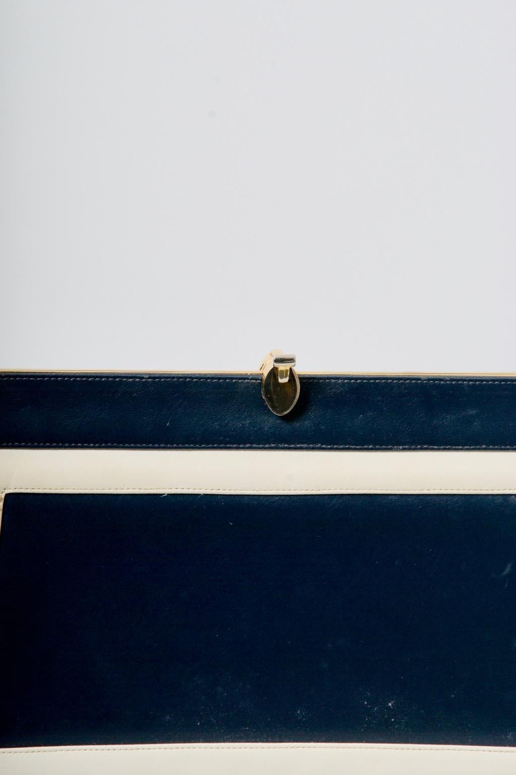 Navy convertible clutch, the exterior enhanced front and back  with a set-in white rectangular border echoing the shape of the bag. The bag features interesting gold tone hardware, including the screw-on latches through which to attach the matching