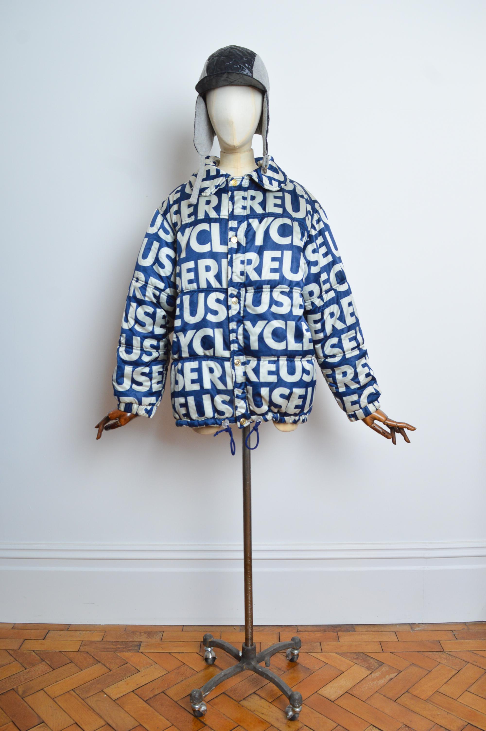 Giacca Bomber Puffa in raso Franco Moschino REUSE / RECYCLE in blu notte e bianco con slogan ripetuto.
MADE IN ITALY.
Taglia 42 di petto - meglio se di taglia media.
Unisex Indumento. 
Le misure sono indicate in pollici ('')
Da fossa a fossa: 23,5