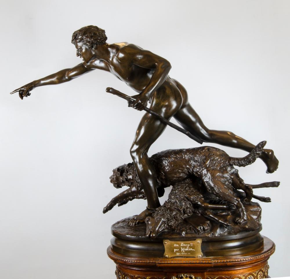 A patinated figural bronze statue (“Chase the Wolf”), by French artist Louis Auguste Hiolin (1846-1912). The sculpture depicts a young shepherd and his dog who, after discovering their fallen lamb, are in pursuit of the unseen wolf responsible for