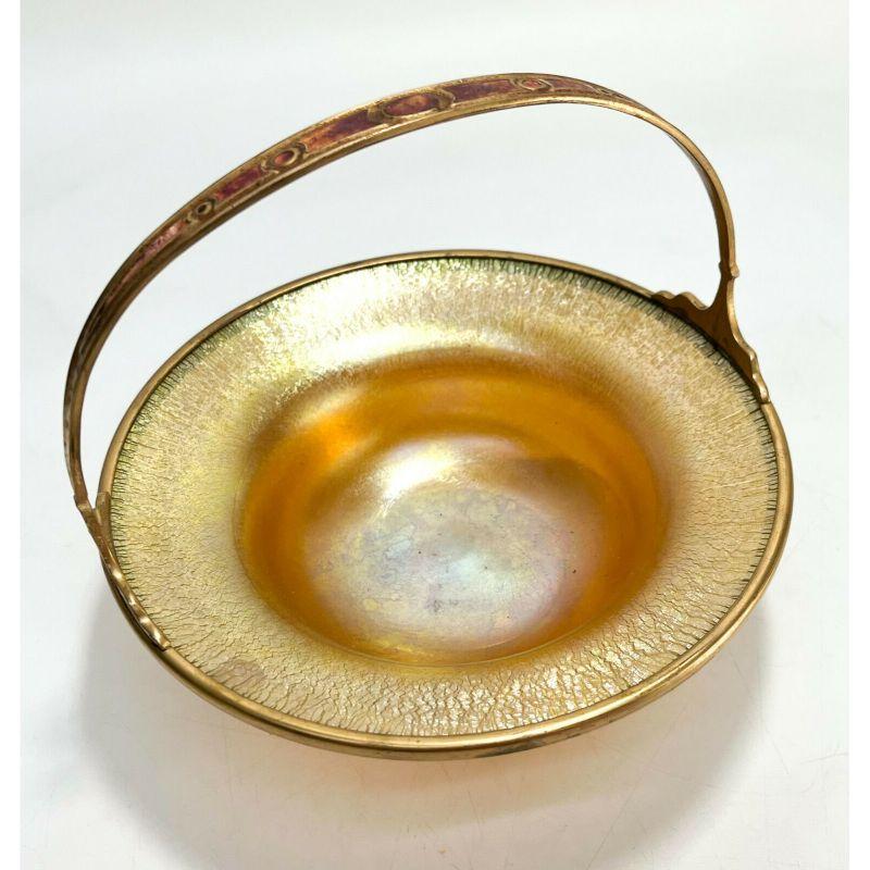 Louis C. Tiffany Furnaces Iridescent Glass Favrile and gilt bronze basket #501

Louis C. Tiffany Furnaces iridescent glass favrile and gilt bronze handled basket #501, circa 1920. Gold iridescence to the glass with hints of blue and pink tones.