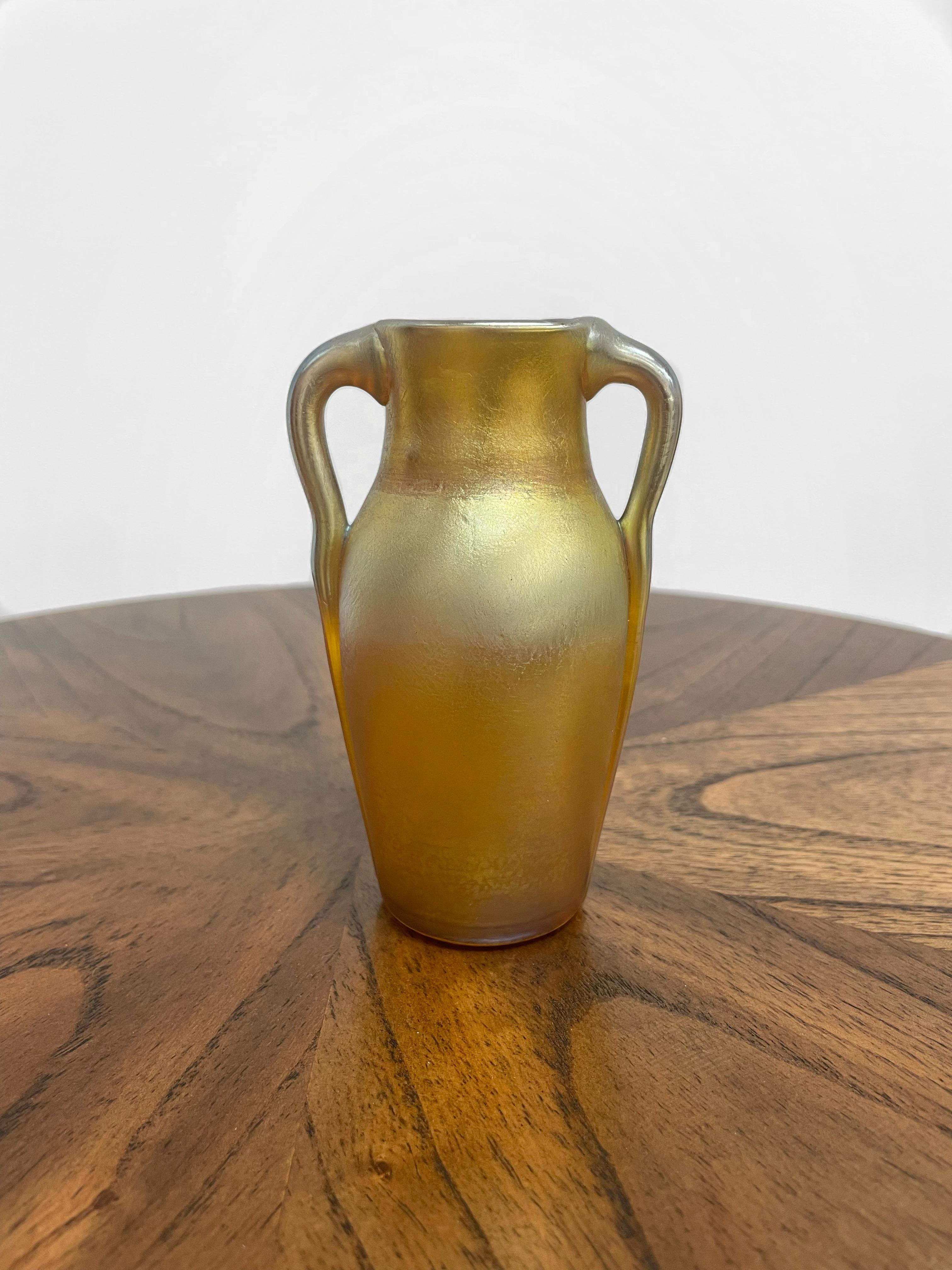 Eine Vase mit zwei extrudierten Henkeln des berühmten Designers Louis Comfort Tiffany. Diese seltene Vase hat eine satte goldene Farbe mit schillernden Highlights in Grün, Blau und Rosa. Favrile-Glas wie dieses wurde 1894 von Louis Comfort Tiffany