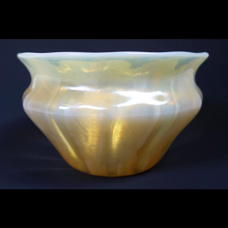 Offering this diminutive Louis Comfort Tiffany gold Favrile and opalescent decorated iridescent art glass bowl. This bowl features a ribbed cinched body with a flared mouth design and is decorated with striated opal glass. Signed on the underneath