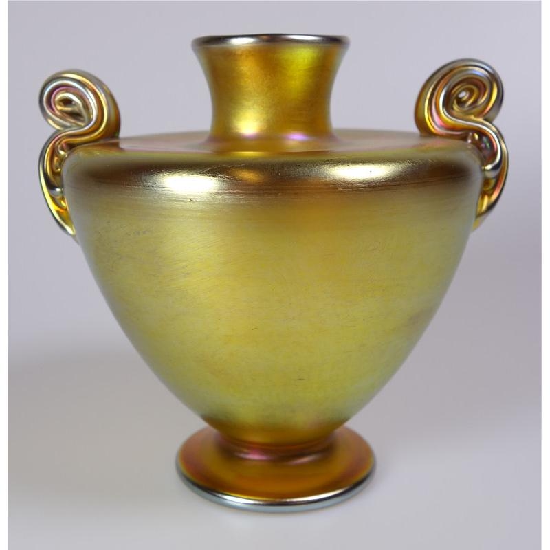 Offering this diminutive Louis Comfort Tiffany gold Favrile iridescent art glass vase. This vase features a ribbed and rolled, double handle design with unusual pinched rim design. Signed on the underneath 