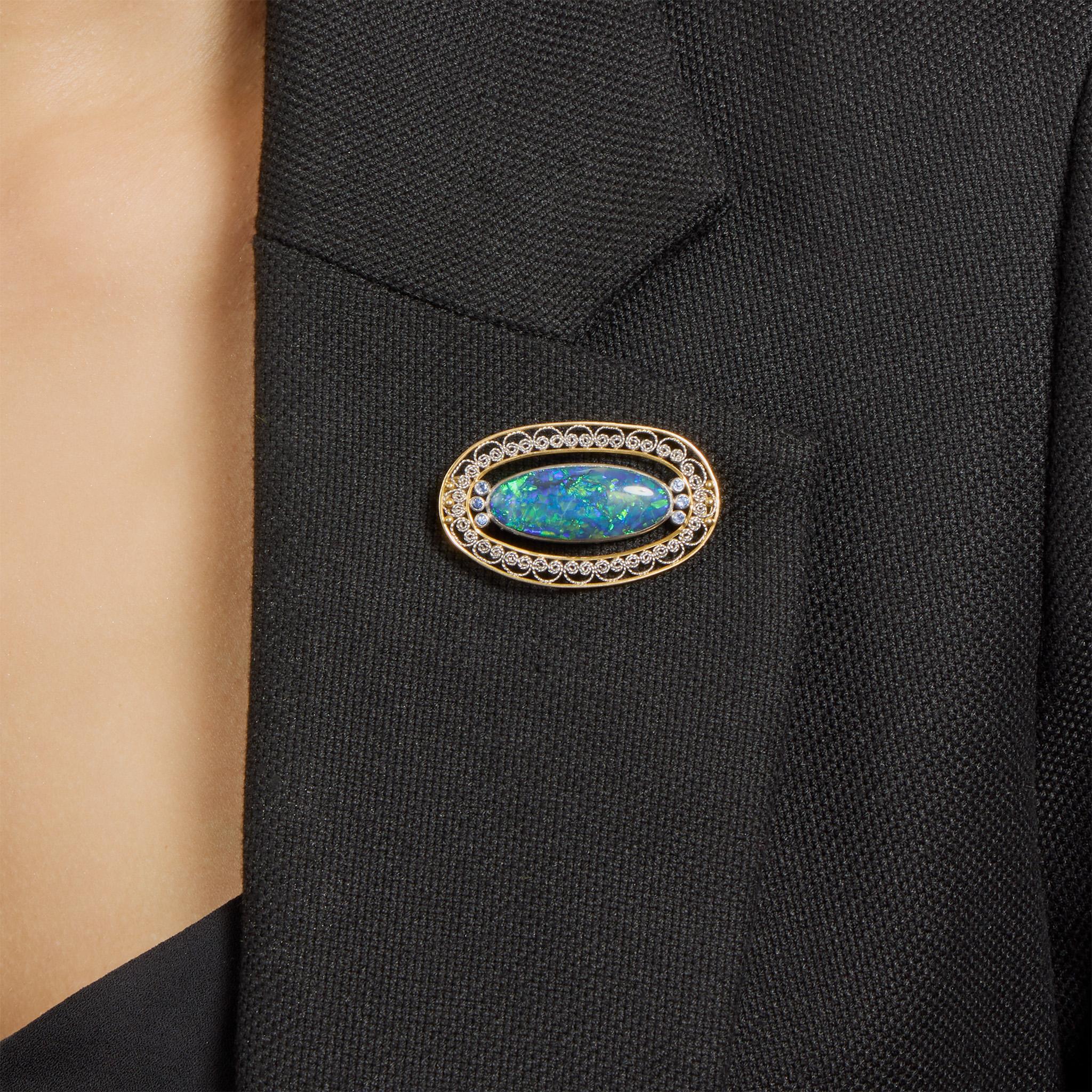 Dating from circa 1915, this 18K gold and platinum brooch set with a black opal and Montana sapphires by Tiffany & Co. was designed and created under the direction of Louis Tiffany. It is set with an oval black opal cabochon flanked by clusters of