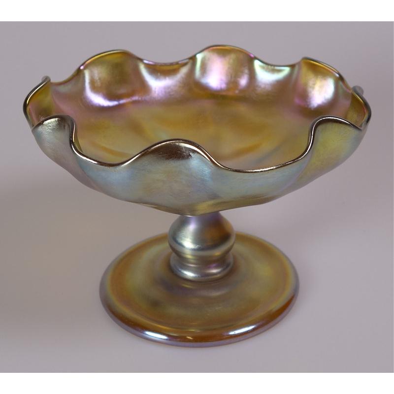 Offering this pristine Louis Comfort Tiffany gold Favrile iridescent art glass compote or footed dish. This compote features a ribbed bowl with a fluted edge attached to a bulbous stem and round foot. Signed on the underneath 