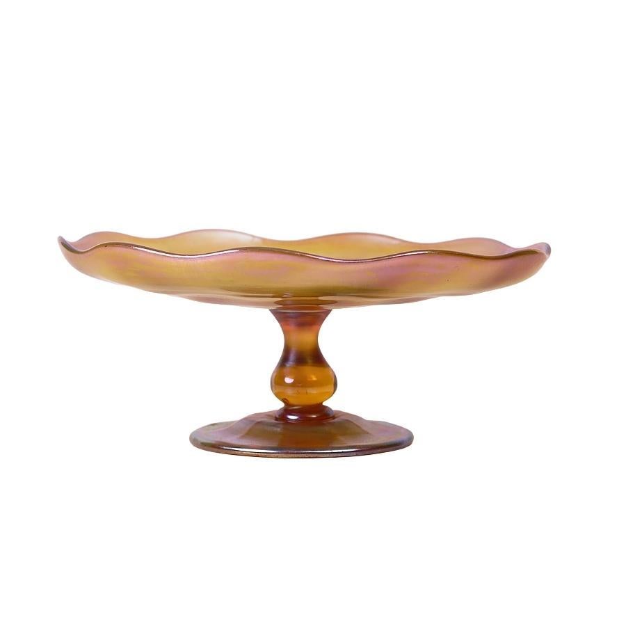Offering this large Louis Comfort Tiffany gold Favrile iridescent art glass compote or footed dish. This compote features a ribbed dish with a fluted edge attached to a bulbous stem and ribbed round foot. Signed on the underneath 