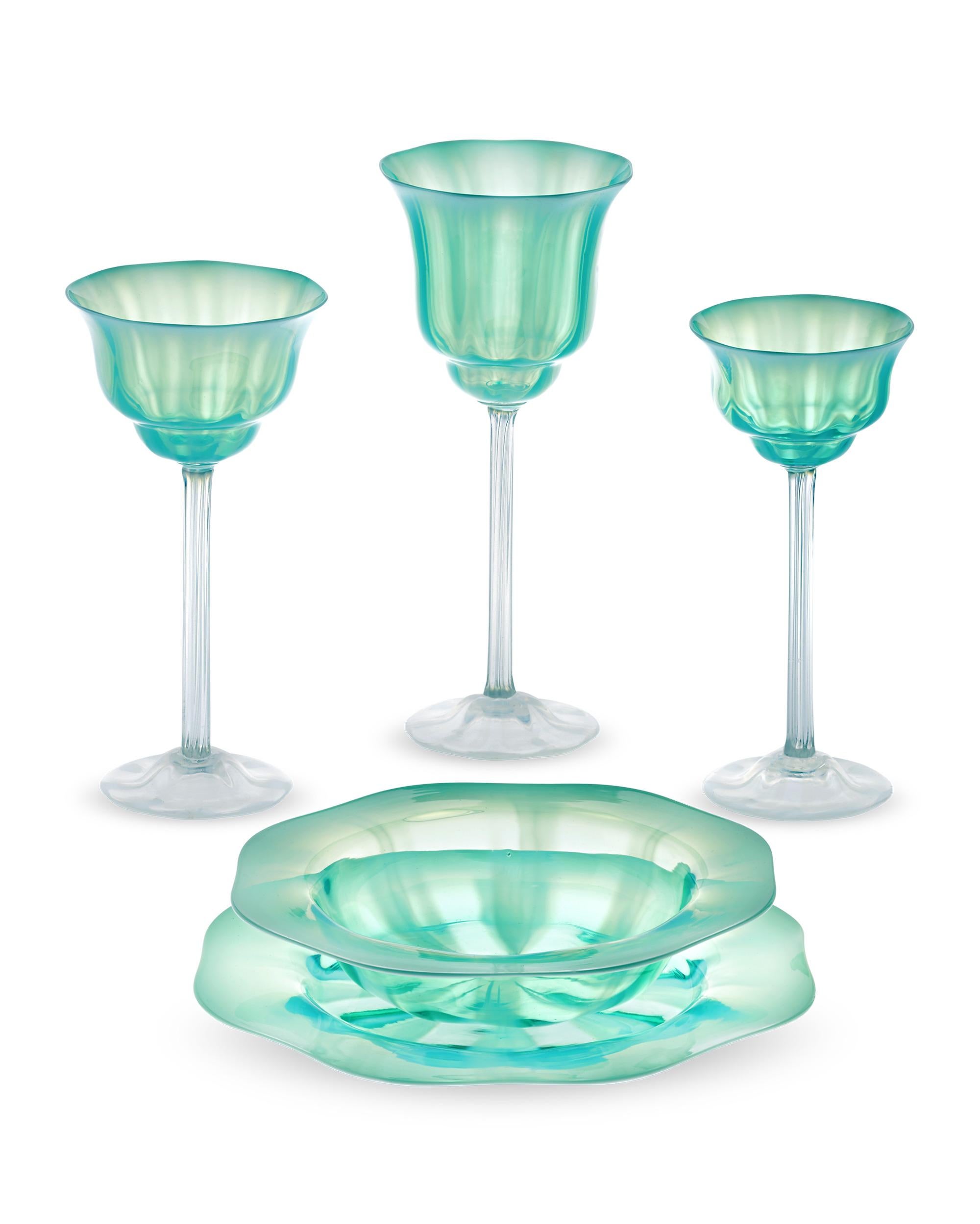 Exuding the elegance of Art Nouveau design, this dinnerware service for 12 from Tiffany Studios is composed of pastel-hued, opalescent green Favrile glass. The plates, bowls and glasses feature a striking light green color with slightly scalloped