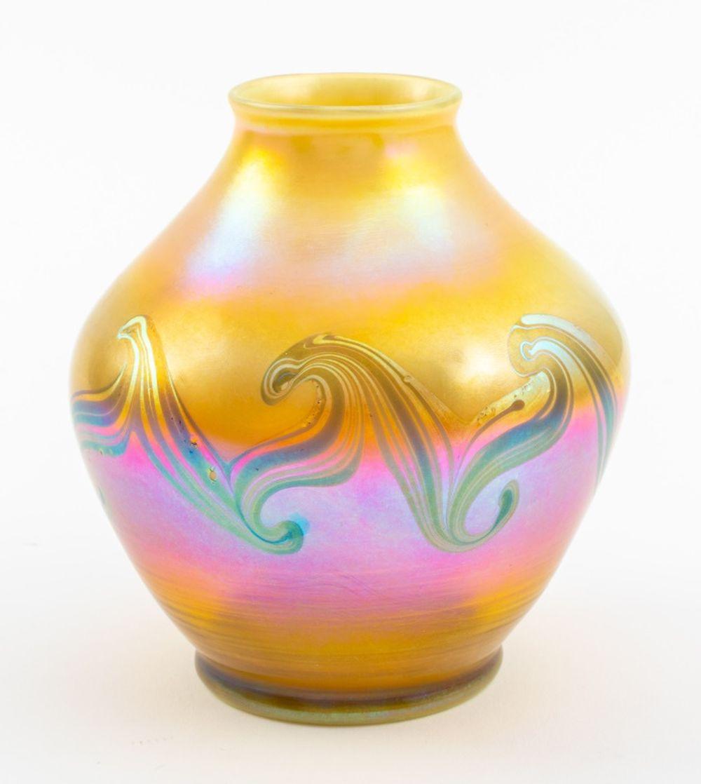Louis Comfort Tiffany (estadounidense, 1848-1933) Jarrón de vidrio soplado reactivo, de forma ovoide entallada con fondo iridiscente sutilmente entonado en dorado, rosa, azul y verde con una banda mediana secundaria de ondas sobre fondo rosa intenso