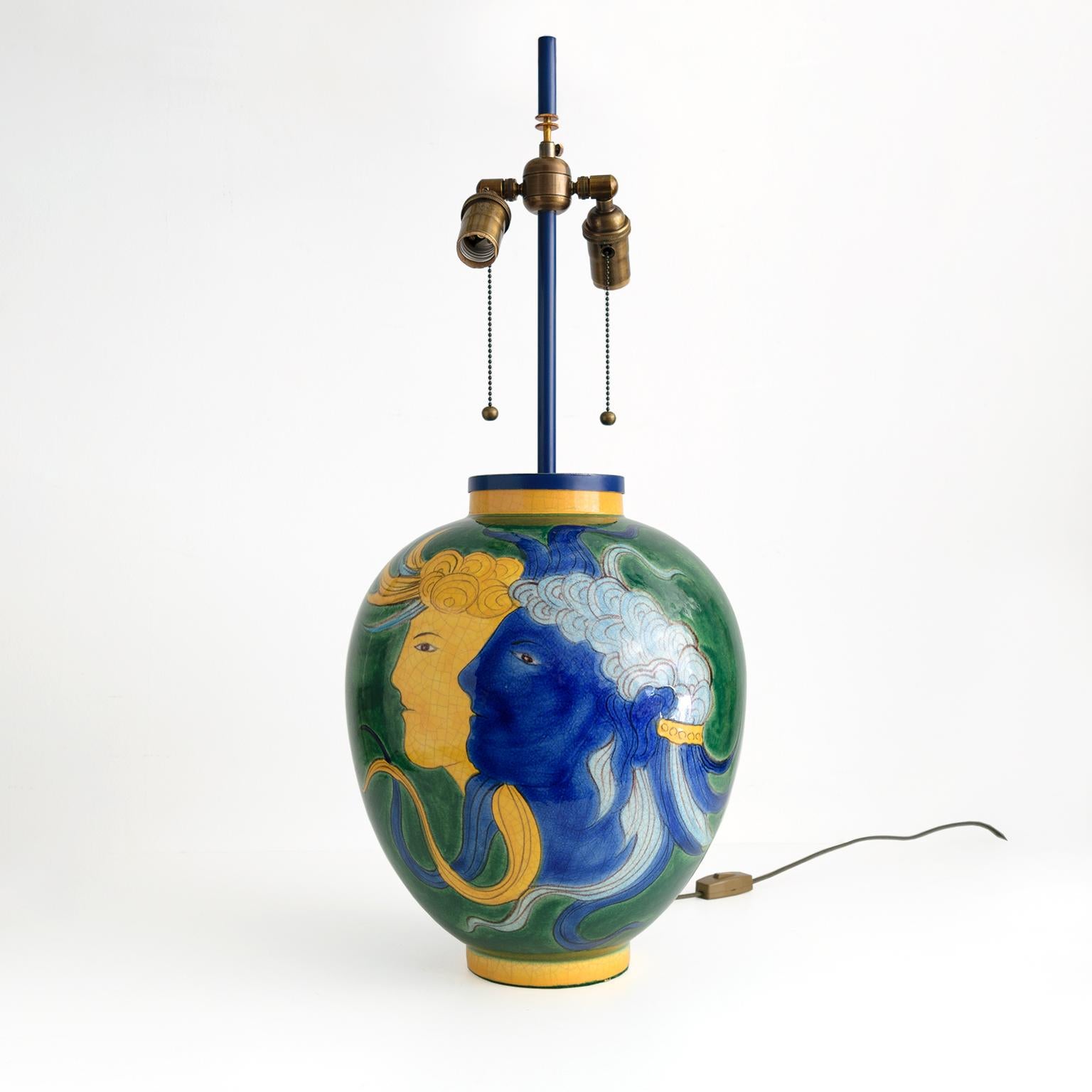 Large, Louis Drimmer ceramic table lamp with a blue and yellow face on a green glazed ground. Newly wired with patinated brass, standard base double cluster sockets. Stem, finial and mounting are custom brass stained in blue, Made in France, 1970.