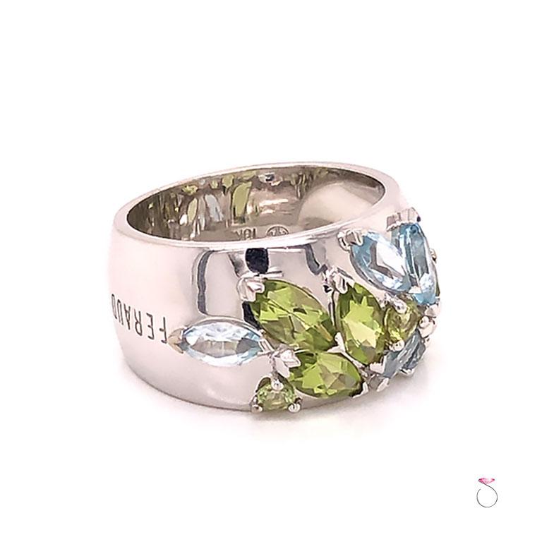 French Designer Louis Feraud Aquamarine and Peridot Cluster wide band Ring in 18k white gold. This beautifully designed band features a gorgeous cluster of gemstones different shapes and colors. The gemstones are marquise and round brilliant cuts