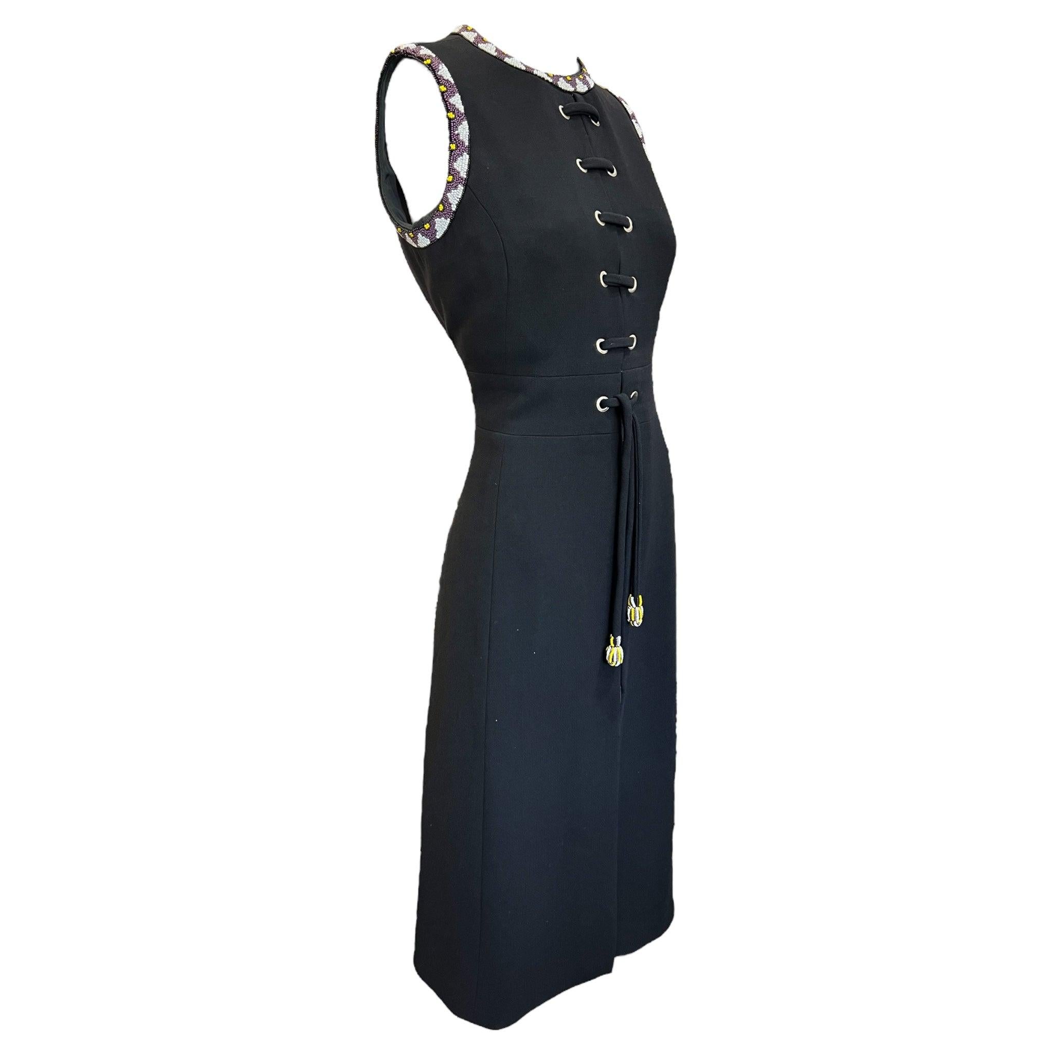 Chic with an edge, 1970's lace-up dress by Louis Feraud. Black wool crepe sleeveless tunic-style dress with jewel neckline and arm holes embellished in white, yellow, and purple seed beads, front bodice lace up detail with waist ties, zippered front