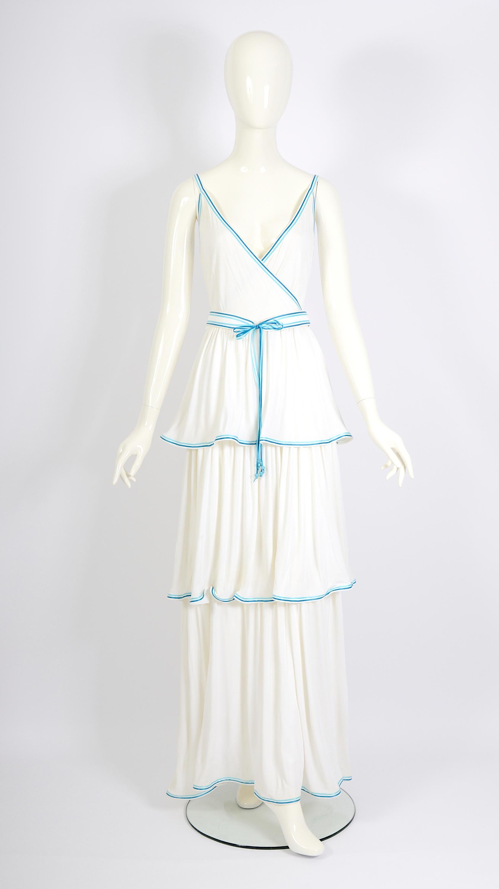 Step into sophistication with this beautiful Louis Féraud vintage 1970s dress, still with tags attached. It's a long, flowing white/cream dress made from soft viscose jersey fabric. The skirt has layers with pretty blue ribbon trim, and the with