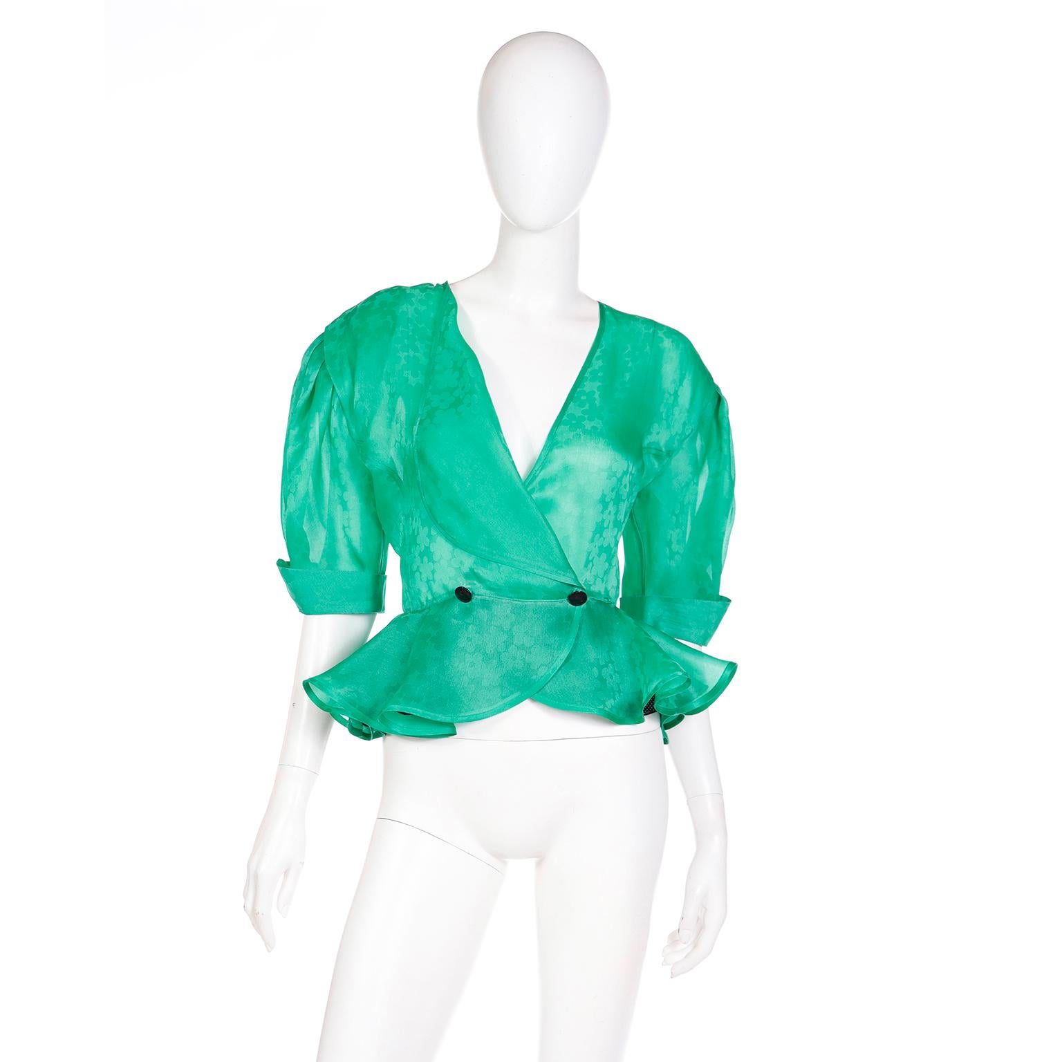 This pretty vintage Louis Feraud green silk organza blouse has a pretty ruffled peplum hem and mid length sleeves with upturned cuffs. This 100% silk blouse is in a tonal floral pattern and has a single row of buttons with snaps at the waist for