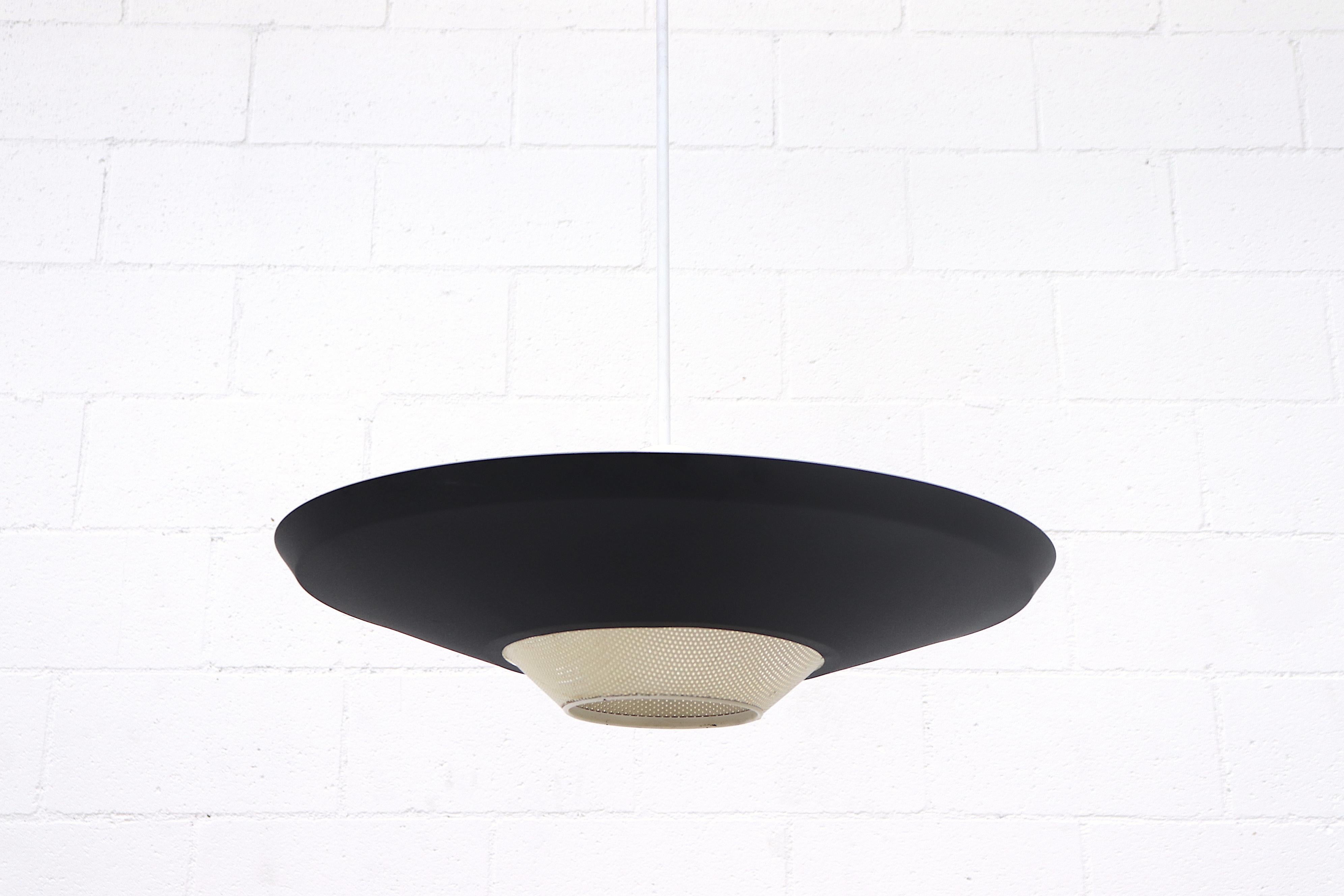 Original black enameled metal Rondelle ceiling pendant. Black enameled shade with perforated bone white accent. Triple light sockets for up-lighting and a single spot for down-lighting. In original condition with wear consistent with its age and use.