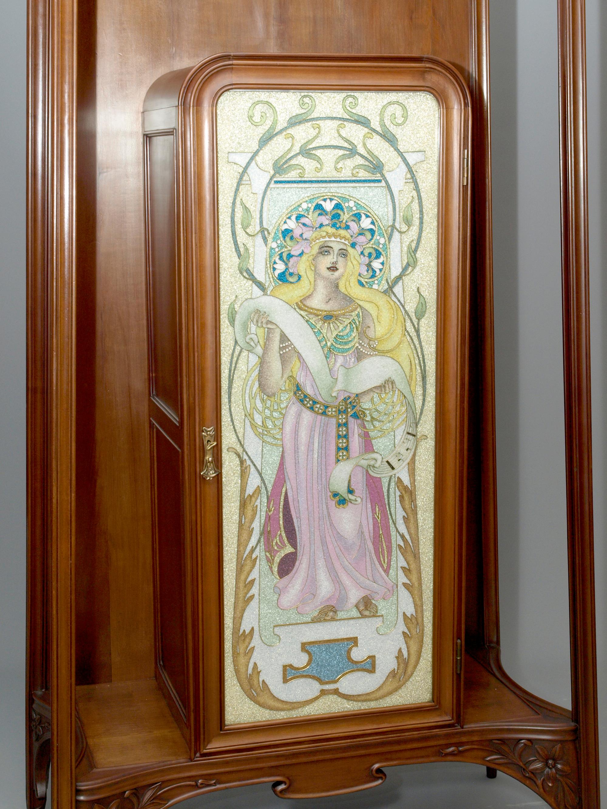 Edler Jugendstil Salonschrank mit floralen Schnitzereien und feiner Cloisonné-Glasarbeit, Louis Majorelle zugeschrieben, Nancy um 1900-1907.

Der Salonschrank besteht aus einem Rahmengestell aus Amerikanischen Kirschbaum, in dessen Zentrum ein
