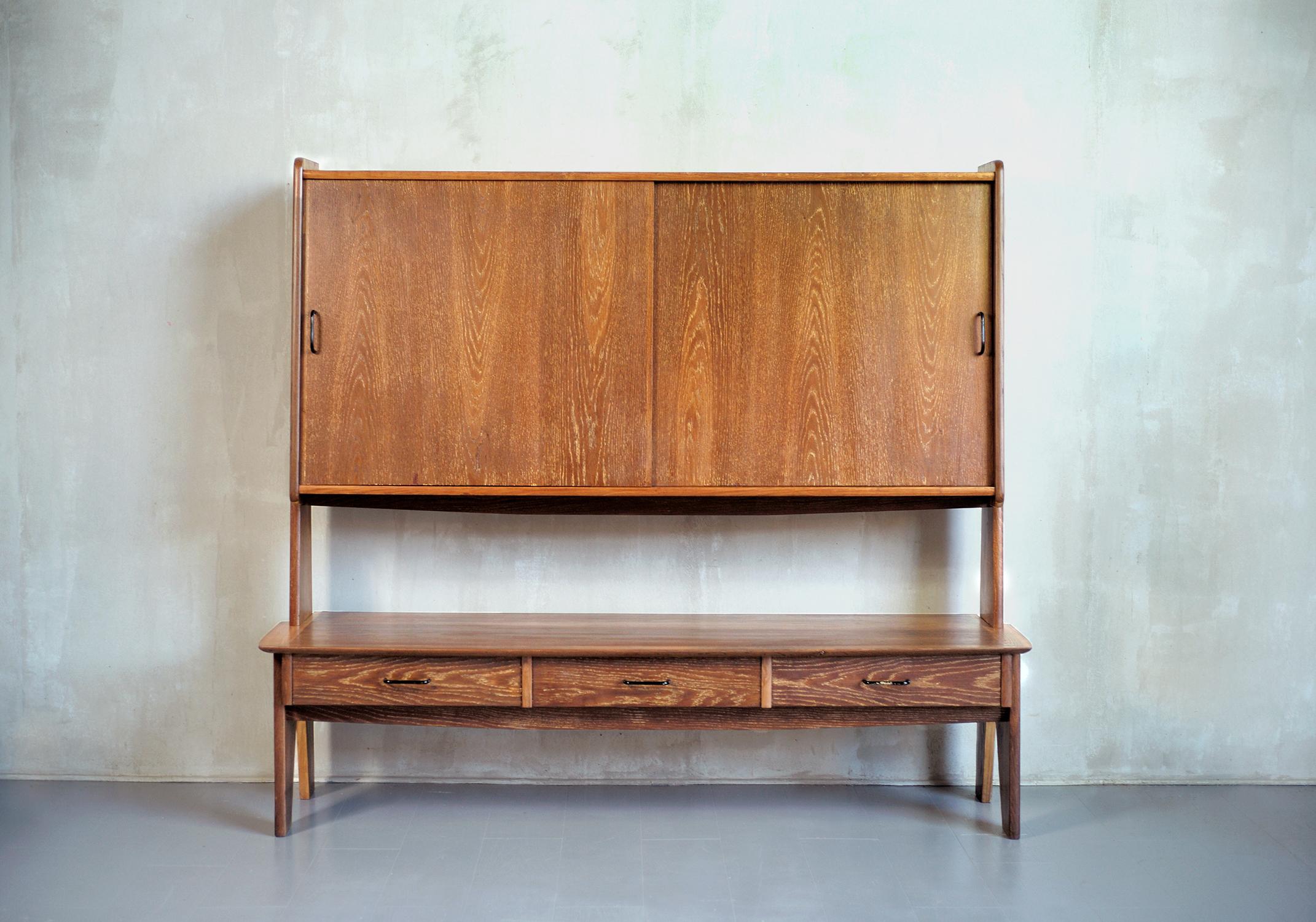 Oak sideboard by Louis Paolozzi, edited by René Godfrid, France 1950. On trapezoidal uprights are set a box with three drawers and a large box with two sliding doors in the upper part. The veining of the oak, highlighted by a light white lead,