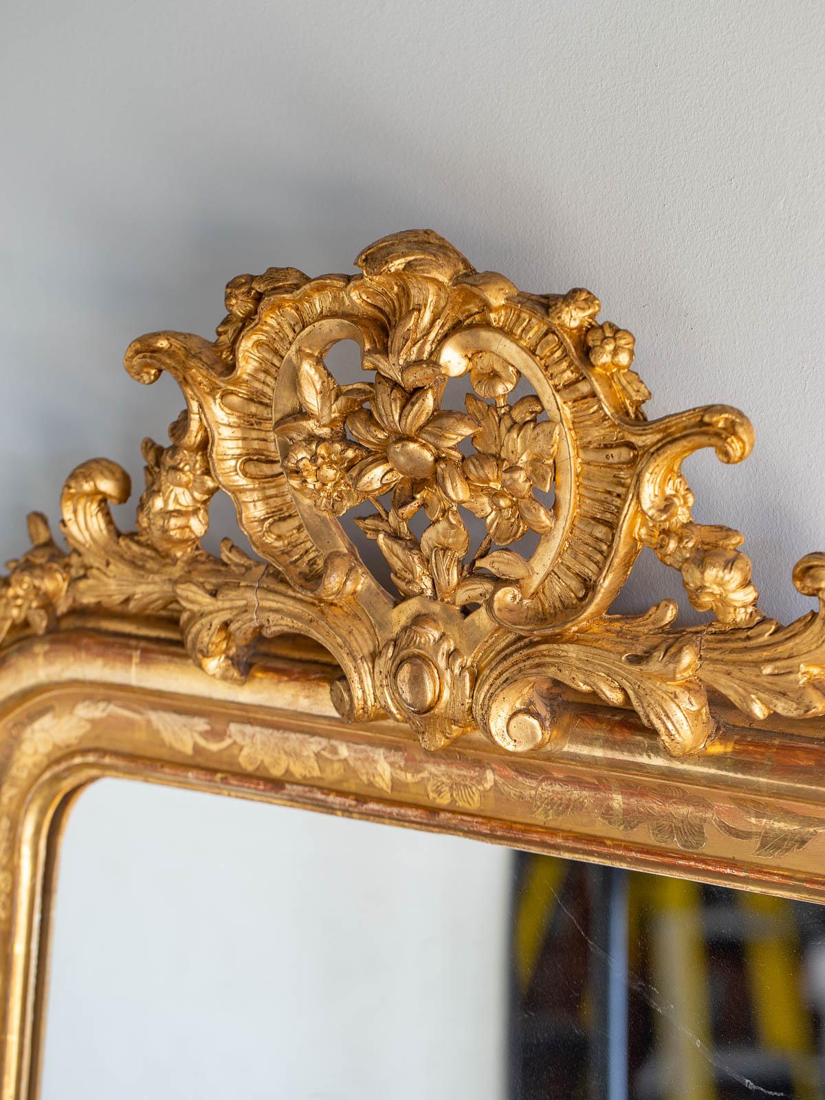 A beautiful antique French Louis Philippe gold mirror, circa 1885 featuring a bold cartouche and the original mirror glass. The elegant minimal frame with its upper rounded corners is embellished with an incised floral design that provides a
