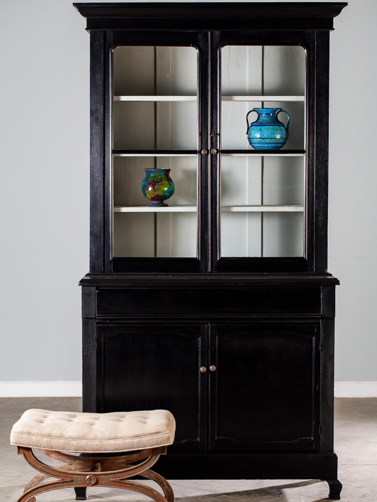 An unusual painted antique French Louis Philippe mahogany bibliotheque display cabinet bookcase, circa 1870. The upper crown has a flared profile that extends forward and to both sides of the top while beneath the crown there are two cabinet doors