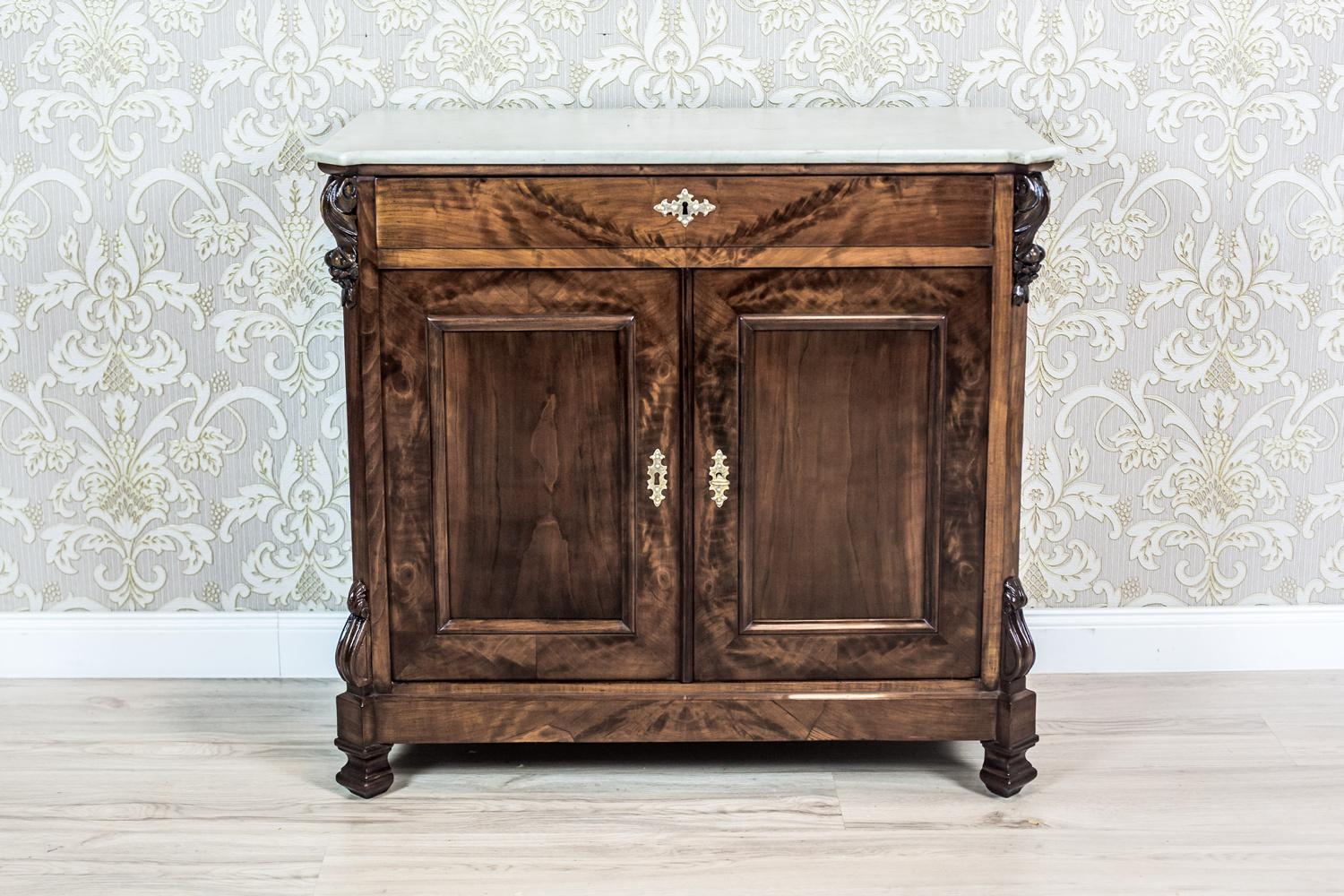 We present you this cabinet piece of furniture covered in noble mahogany veneer, with a top made of white marble.
The cabinet is two-door, with a wide drawer under the top.
Furthermore, the corners are cut, decorated with layered semi-plastic