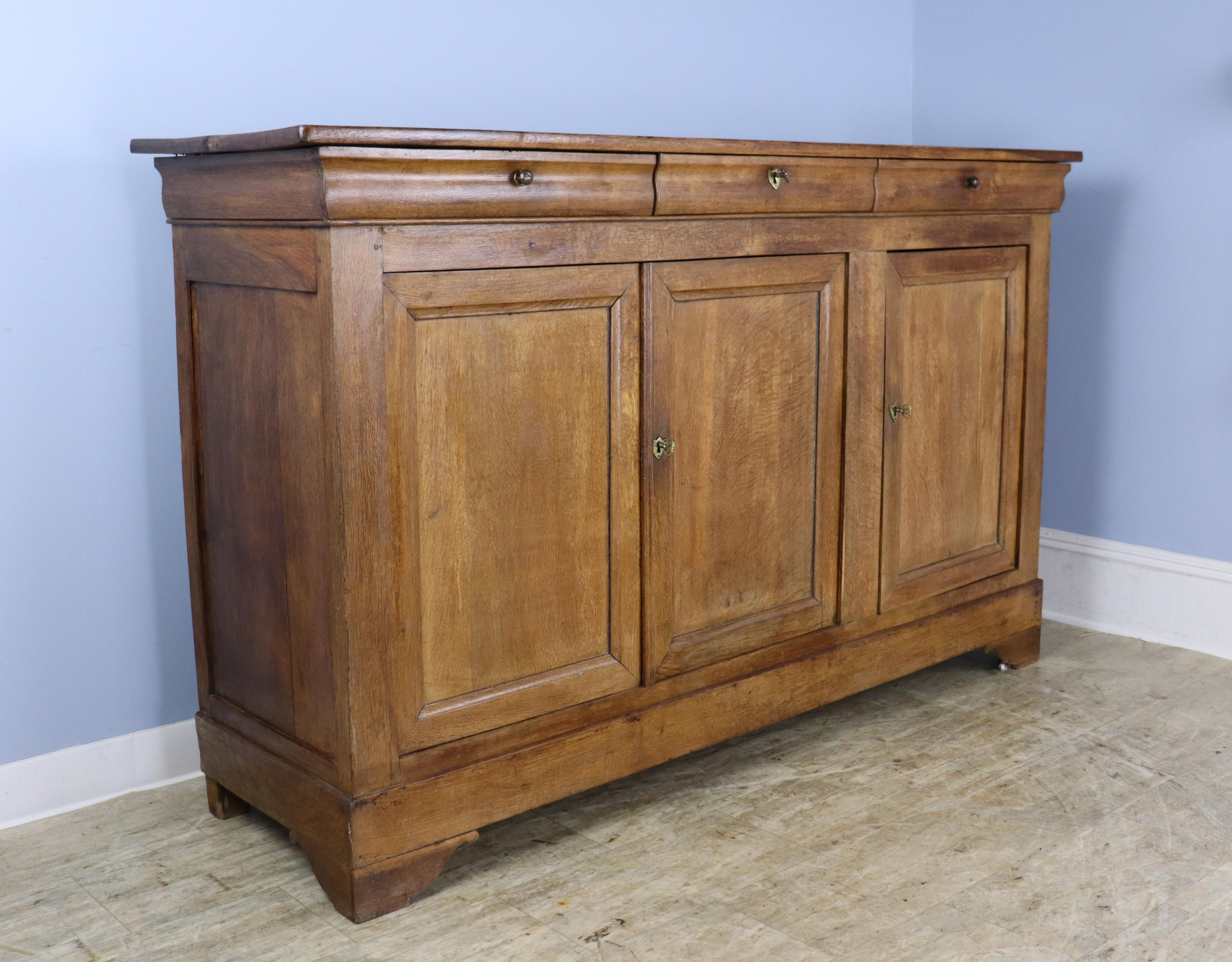 Very good, medium brown chestnut three-door enfilade, buffet or sideboard with beautiful grain highlighted by well colored inset panels on the doors. Glorious glow and patina. Nice stylized feet. The brass hardware original and fullof character. 