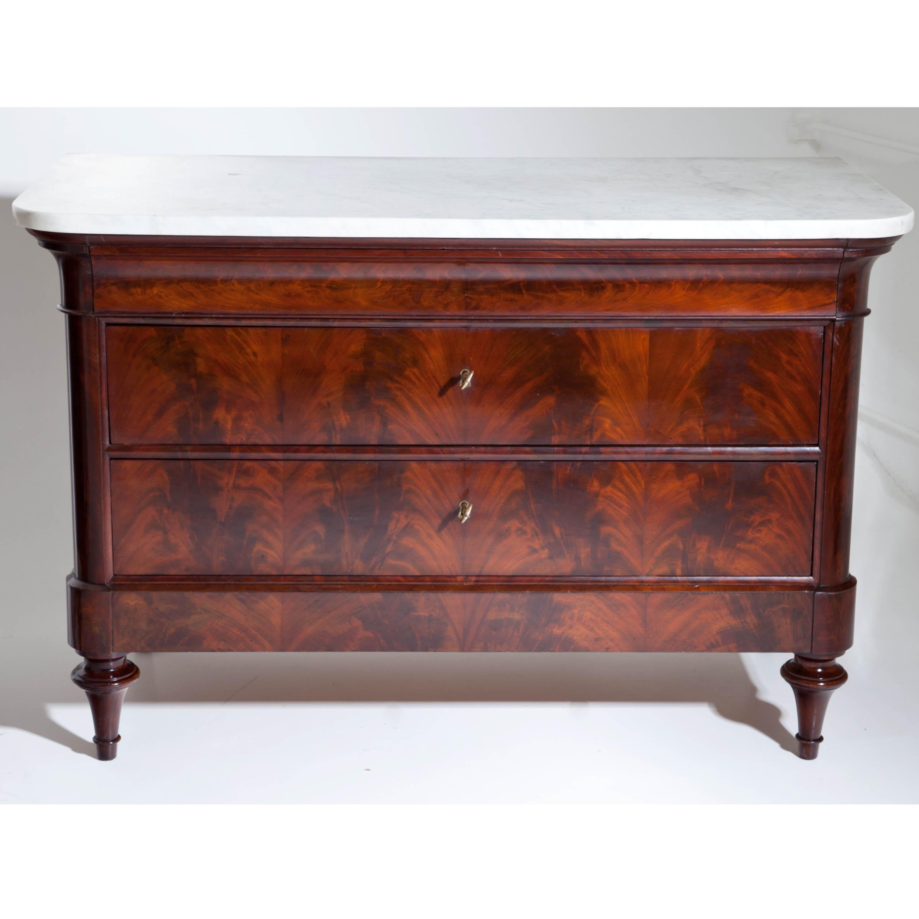 Pair of Louis Philippe chests of drawers on conical feet. The body with rounded corners and three drawers with flamed mahogany veneer and slightly protruding cornice. The tops are white marble.
 