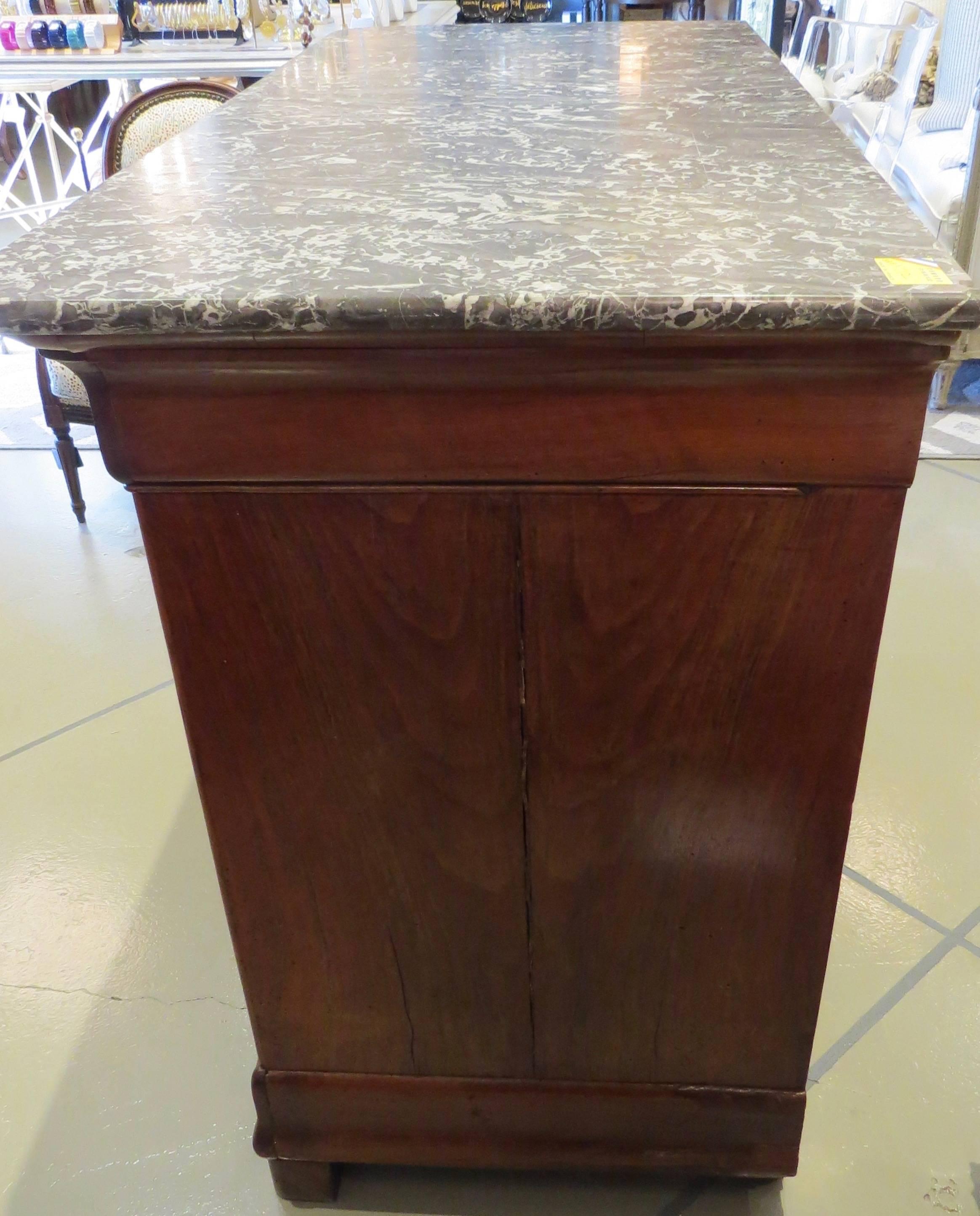 This French commode has four drawers and a marble top. The wood is stained. A key locks the top drawer.