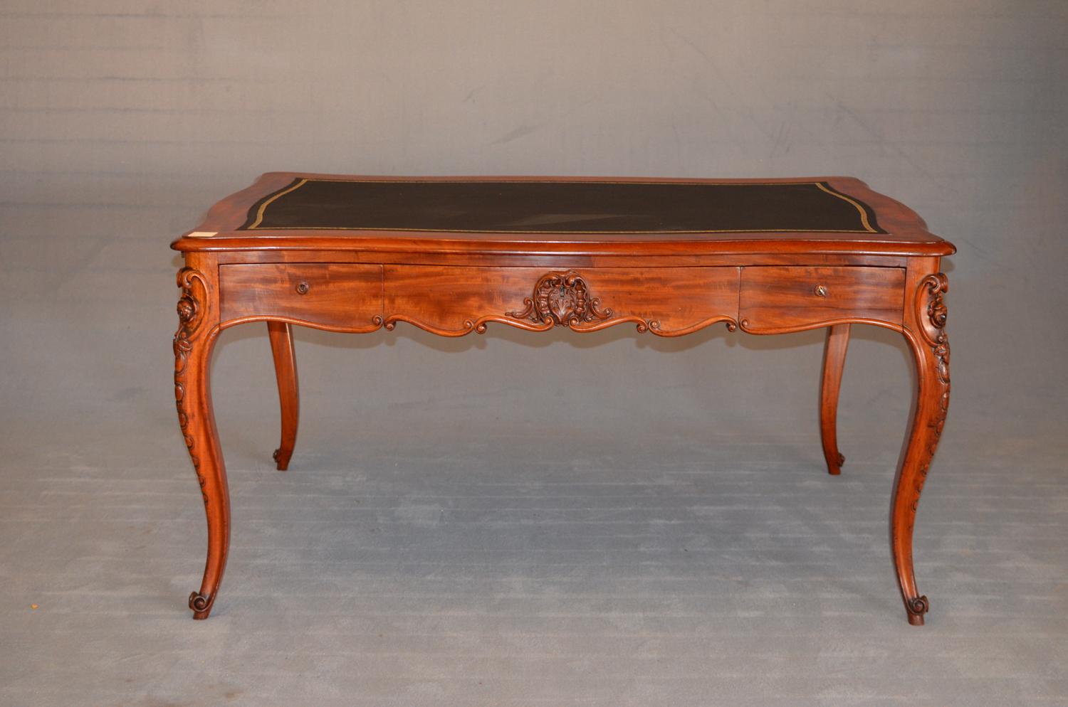 This Louis Philippe wooden desk in mahogany was produced in France at the beginning of the 19th century. The desk is equipped with drawers on both sides and extractable shelves on the sides. The shaped top is upholstered in black leather, the charm