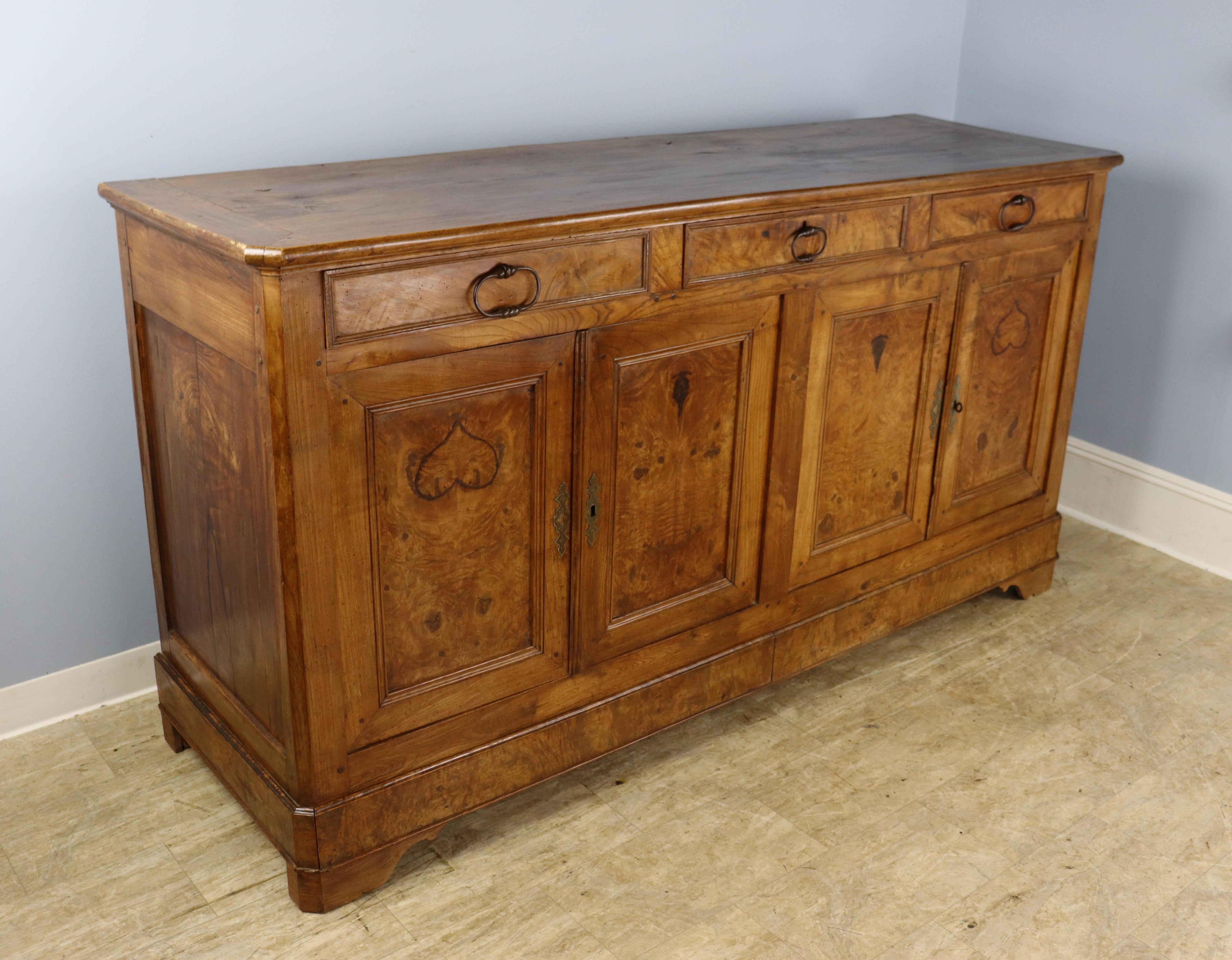 A large four door enfilade or buffet, fashioned out of solid elm burrs. The wood has been matchbooked on the sides, doors and top to charming effect, especially where the grain forms upside down hearts on two of the doors. Wonderful color and patina