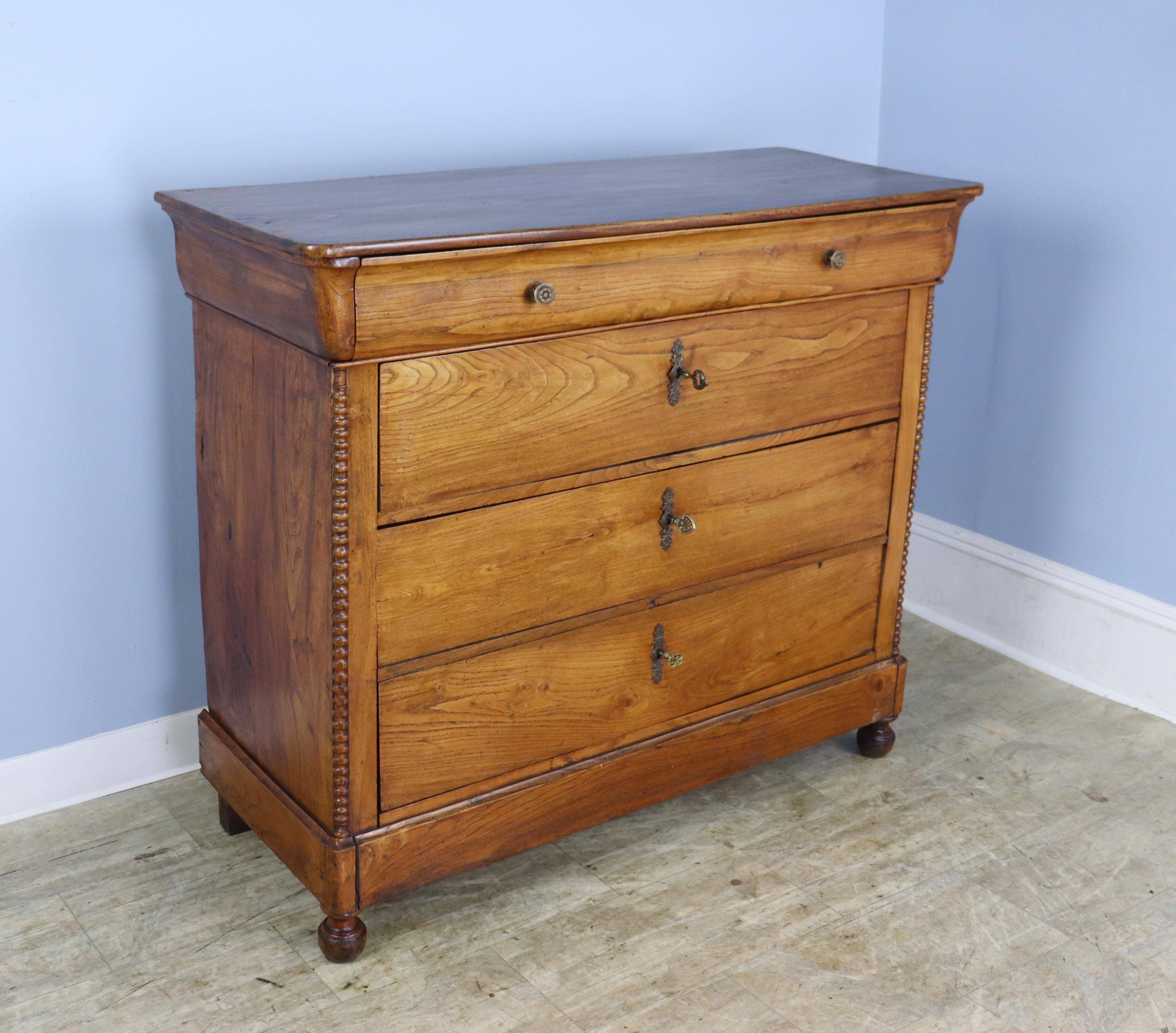 A pretty French elm chest of drawers from the Louis Philippe period with lots of good detail, such as the bobbin turned columns, faux facade top drawer, and stylized ball feet. This piece came without keys, and we have used a mismatched set of three